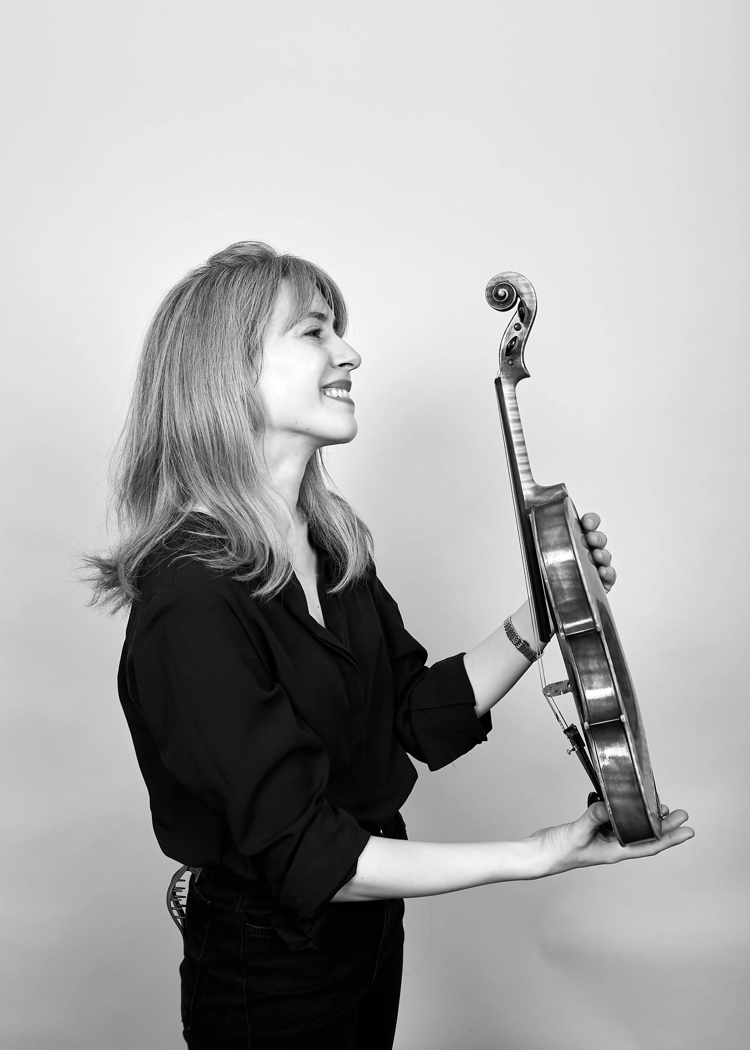 A black and white profile image of violinist Talia Ramos holding her violin in front of her