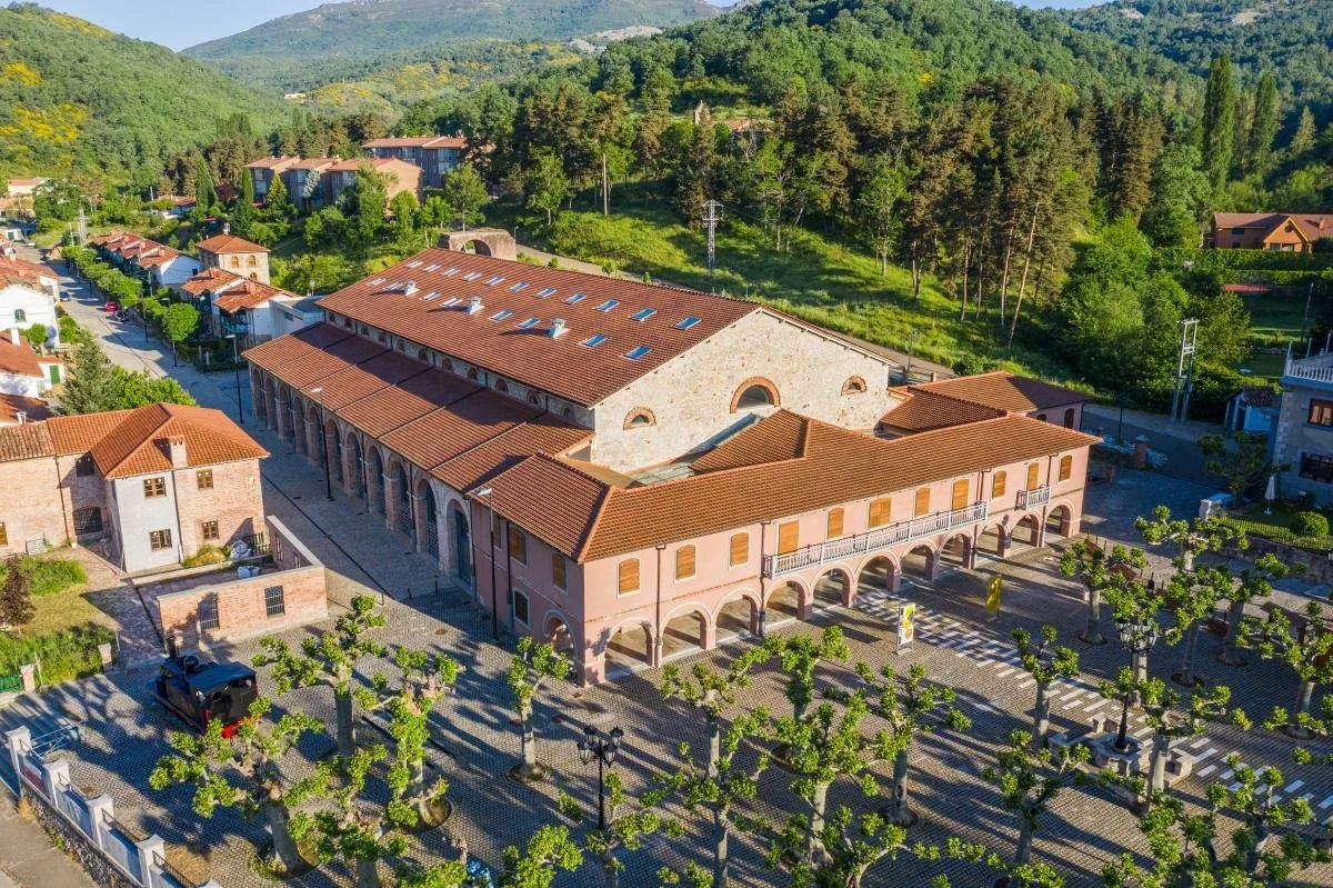The Museum of Iron and Steel and Mining of Castilla y León (MSM) in Sabero, Spain. The image shows the exterior of the building which is surrounded by green trees and mountains in the background.