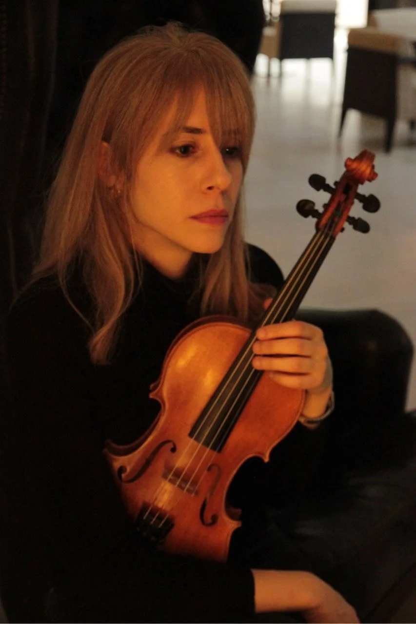 A side profile of a woman, Talia Ramos, holding her violin with a soft, warm light.