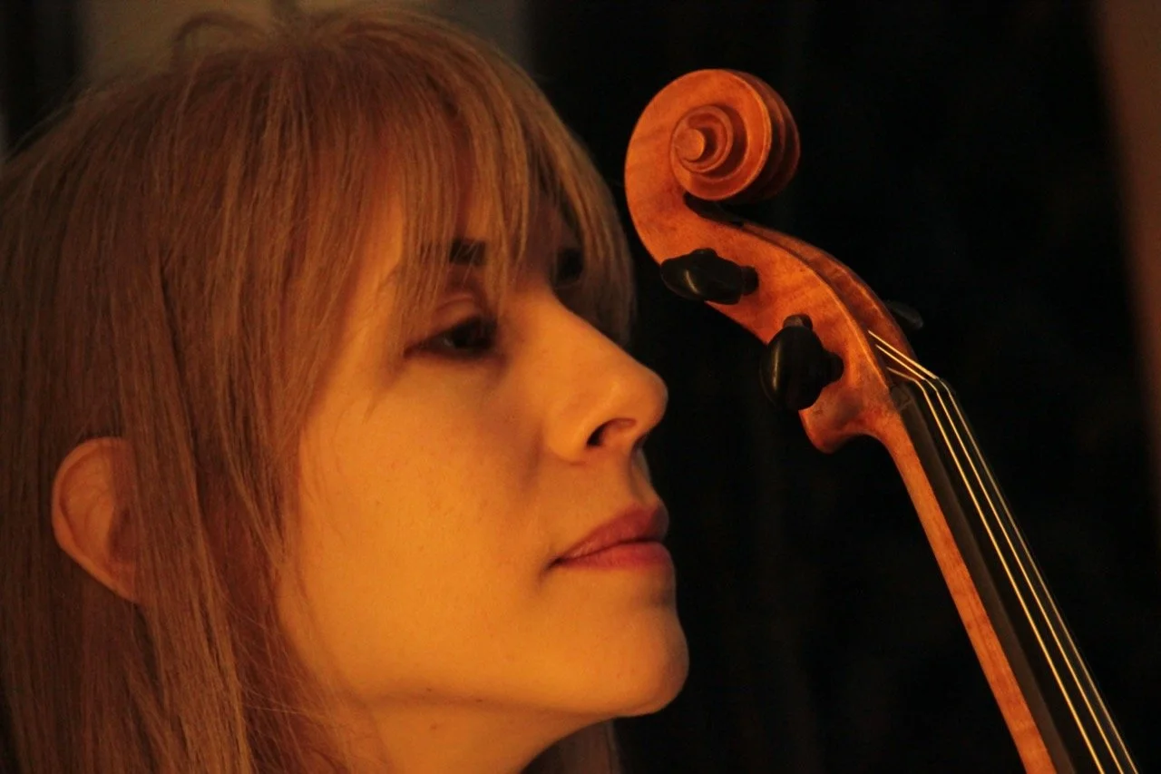 A side close up portrait of a woman, Talia Ramos, looking at her violin with a relaxed face expression and soft smile.