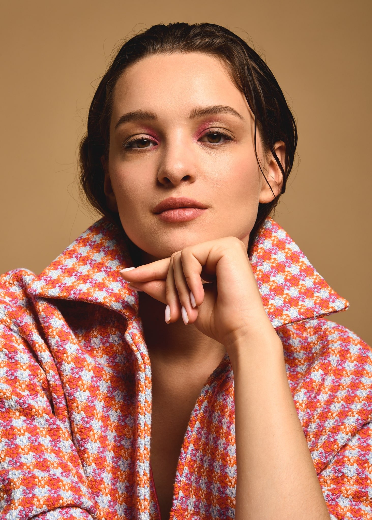 Ritratto di una giovane donna con capelli castani corti, che indossa una giacca a motfici floreale dai toni arancioni, rosa e bianco, contro uno sfondo beige. La donna ha un look naturale con trucco leggero, con sopracciglia folte e labbra neutre. St