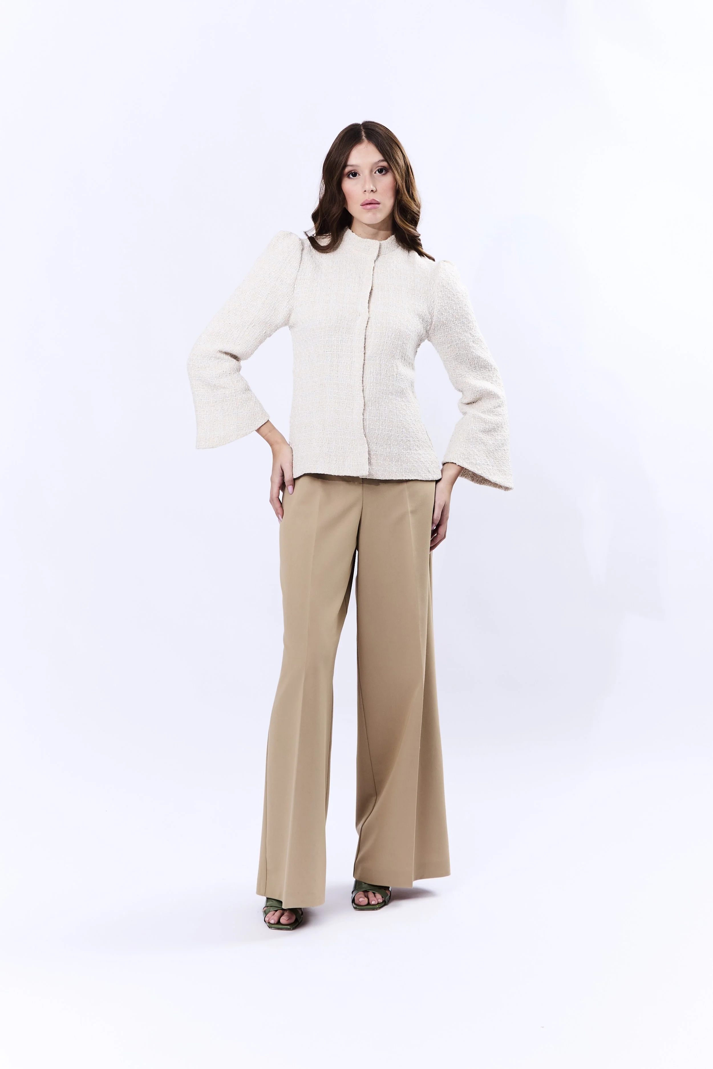Donna elegante con giacca chiara e pantaloni beige in piedi su sfondo bianco.