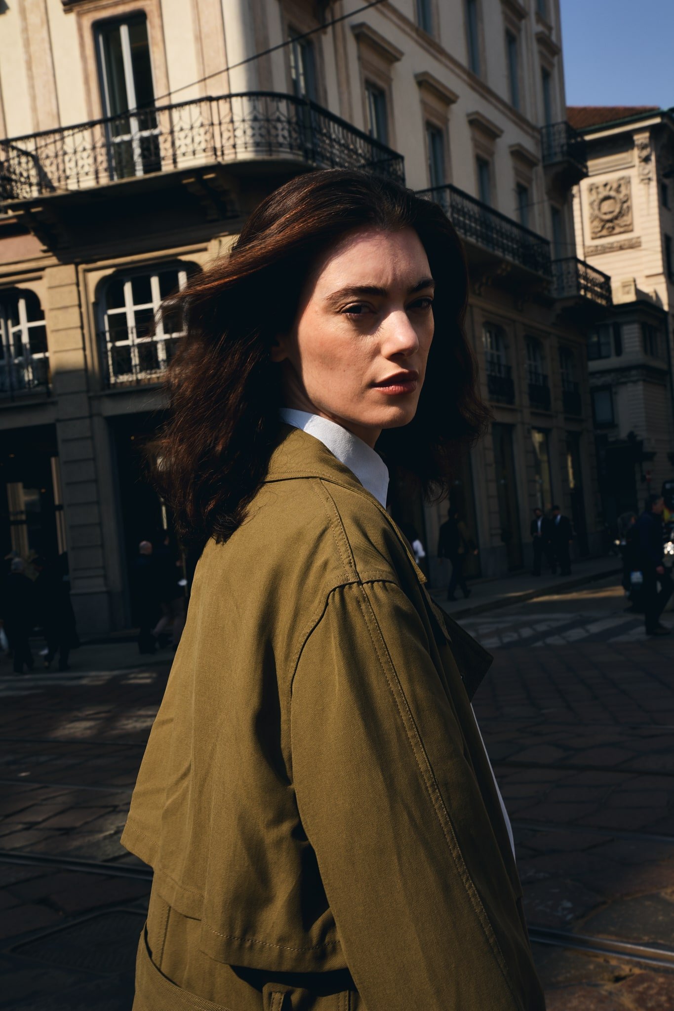 Ragazza con giacca color oliva, sfondo città.