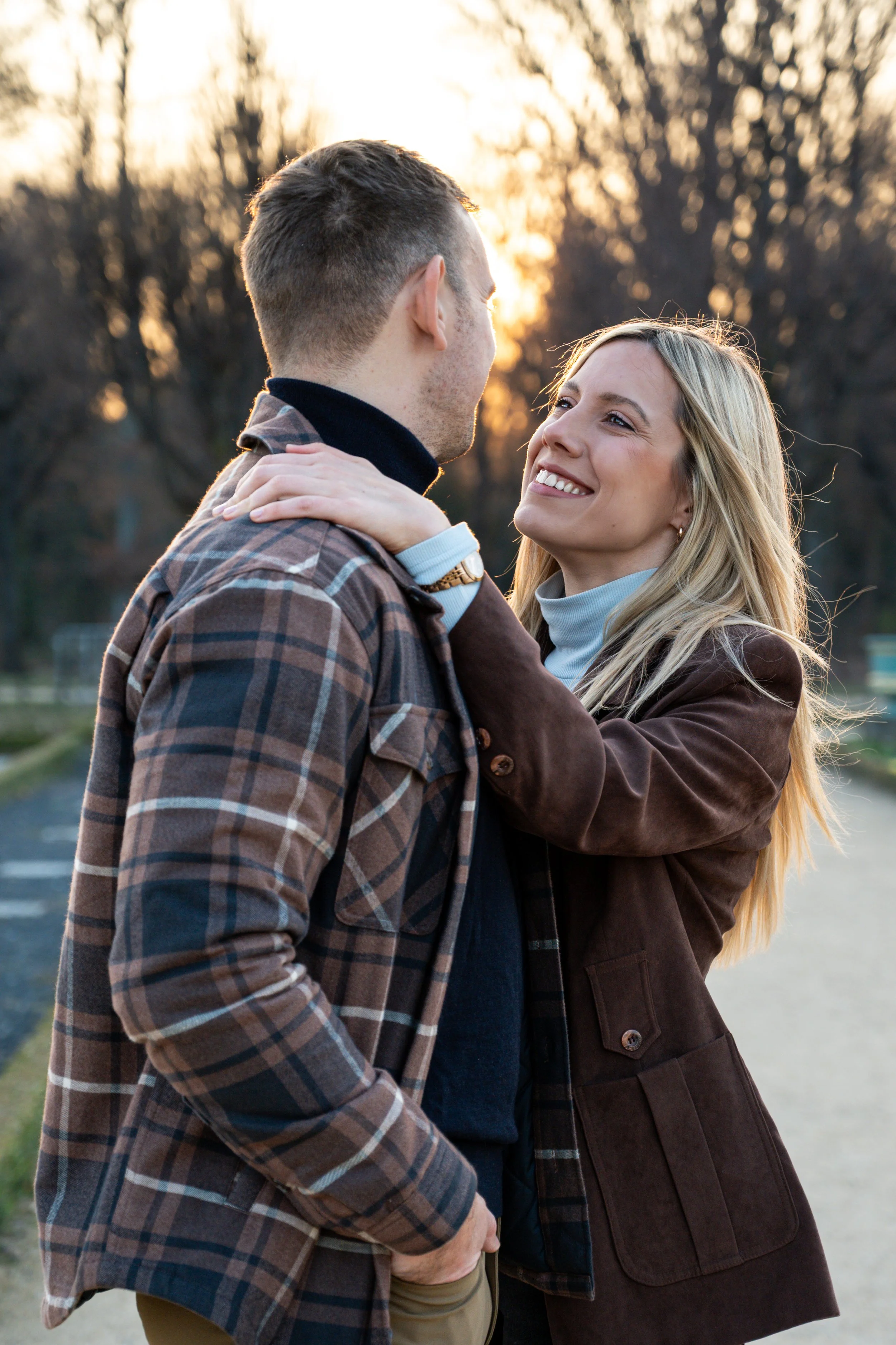 A couple smiling at each other outdoors during sunset, with trees in the background.
