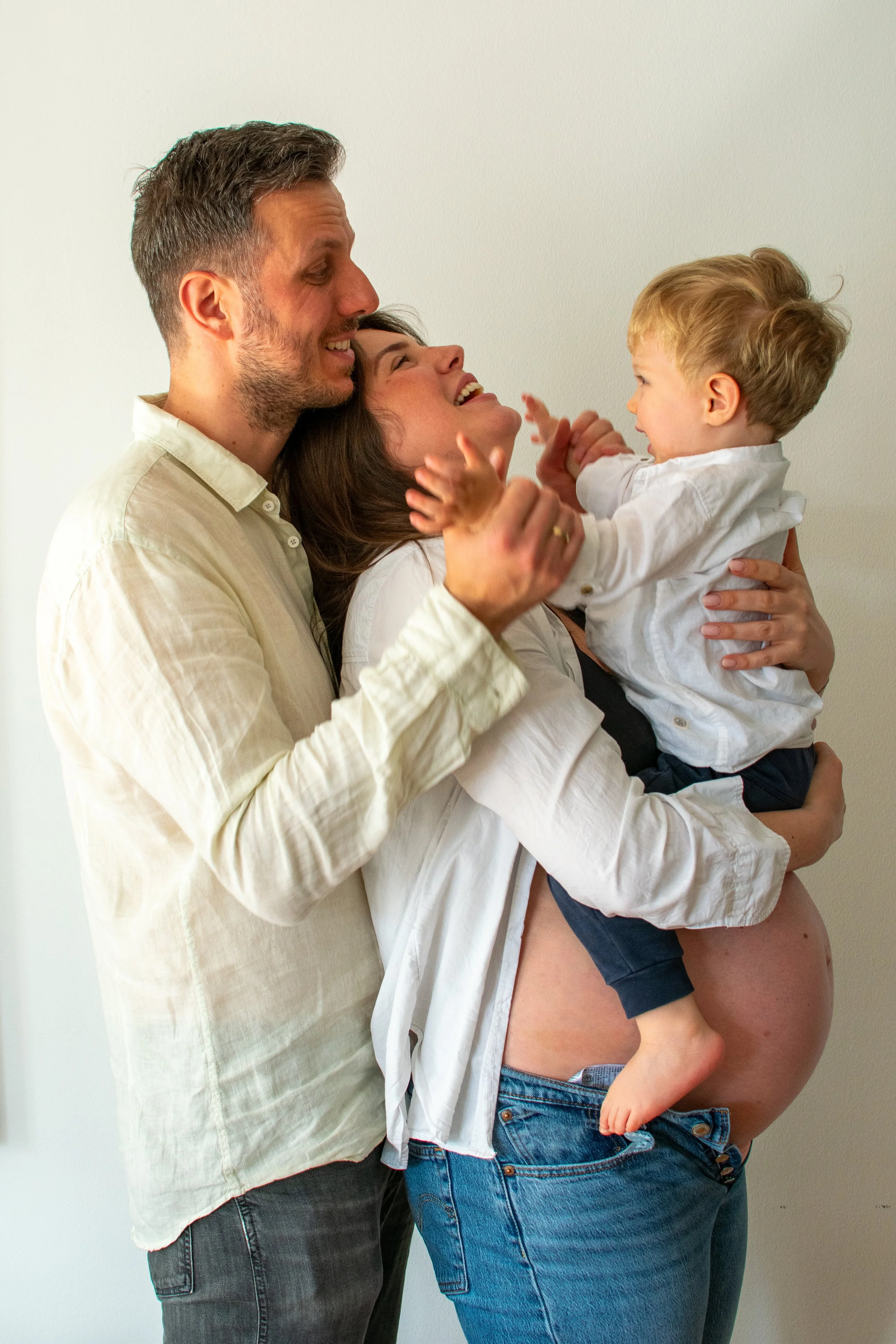 A happy family of three, including a pregnant woman, a man, and a young child, sharing joyful moment together.