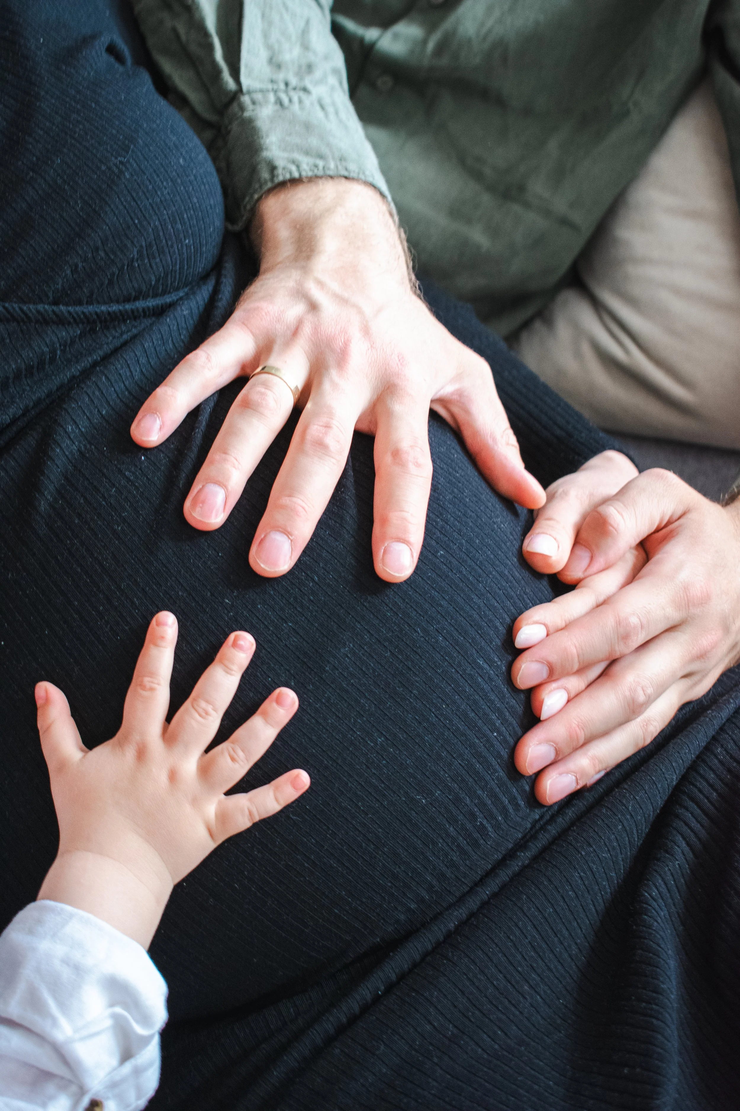 Close-up of a person’s hand resting on their pregnant belly, with a young child’s hand reaching out to touch it.