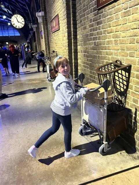 Young girl with a shopping cart in a train station, smiling at the camera.