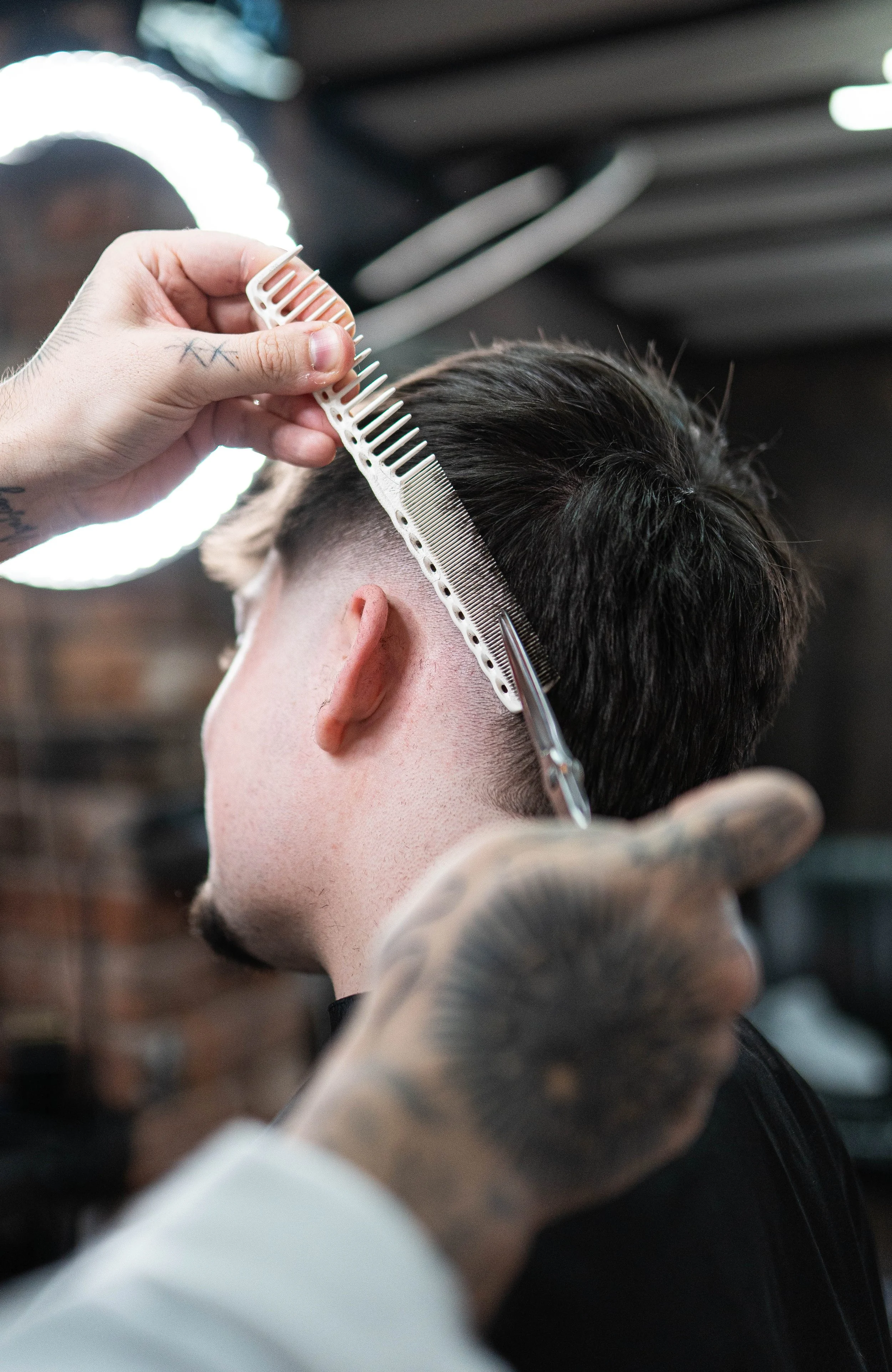 Barber trimming a man's dark hair with scissors and a comb in a salon.