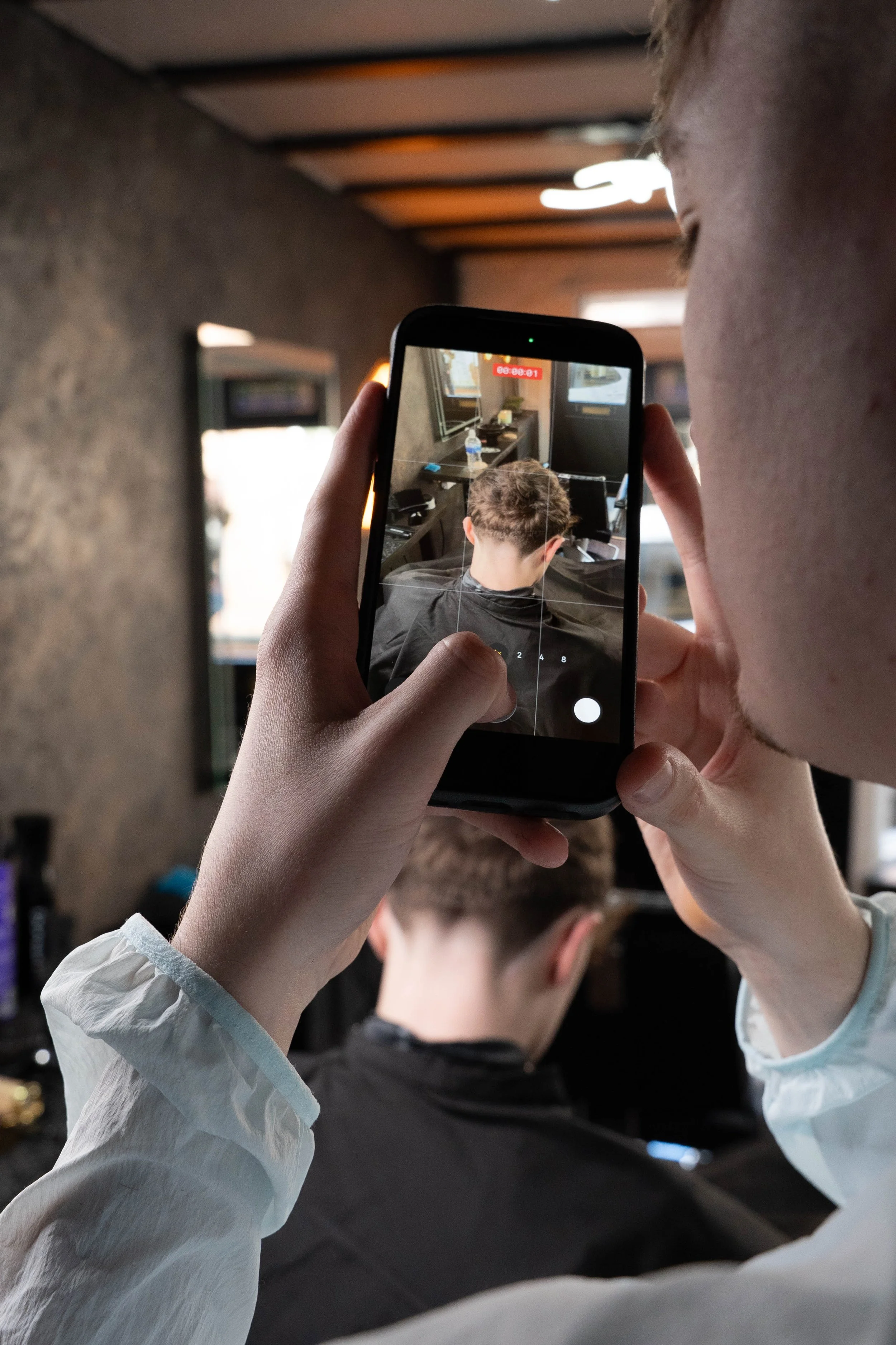 Person taking a photo of someone sitting in a salon chair with a smartphone.