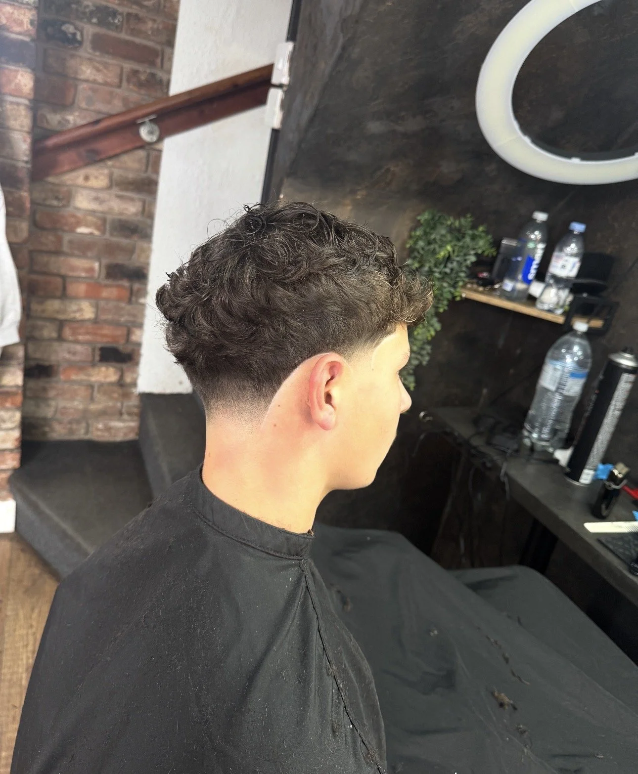 Young man with a short, curly haircut sitting in a hair salon.
