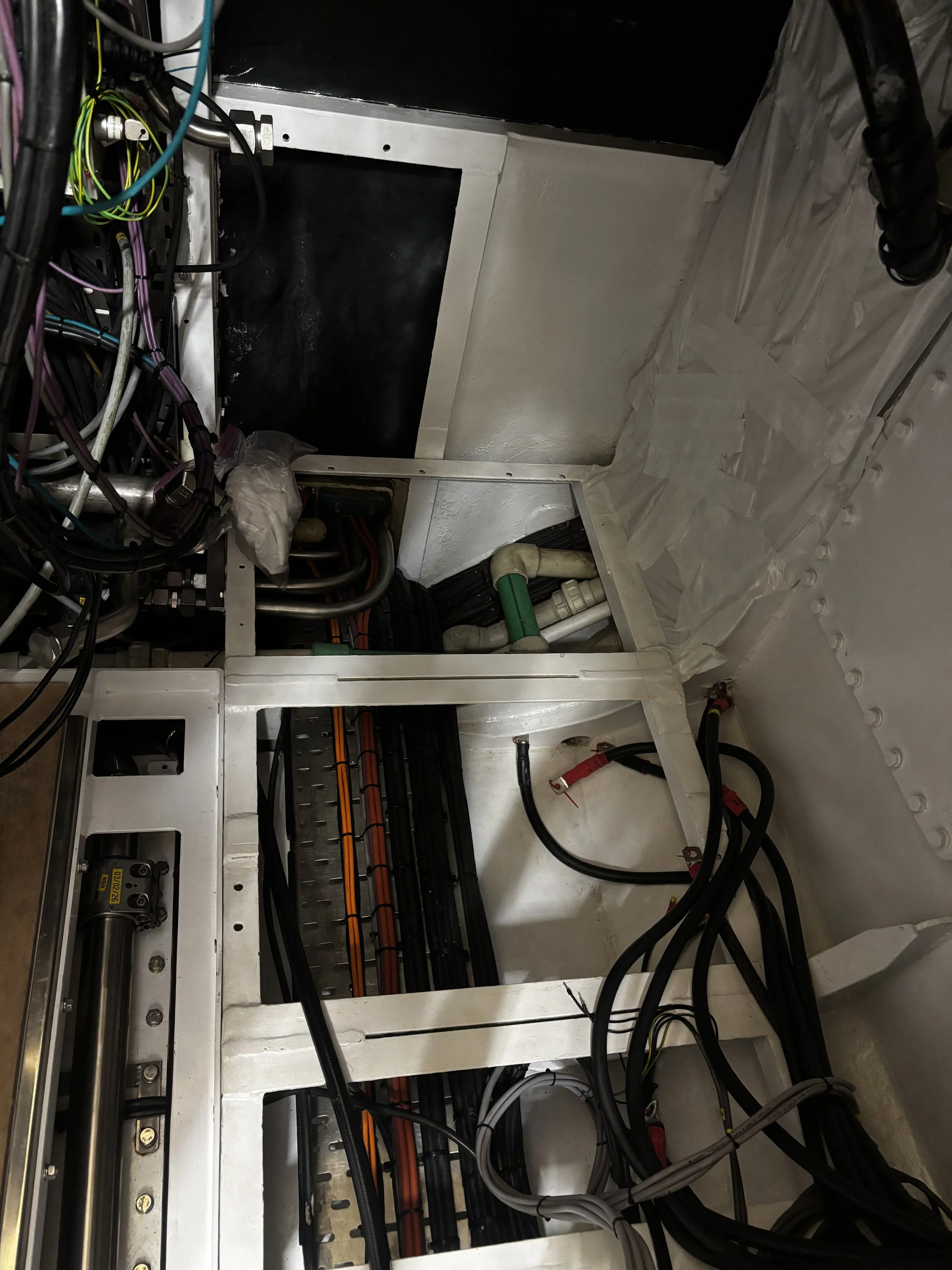 Inside view of an electrical or mechanical panel with wires, cables, pipes, and components.