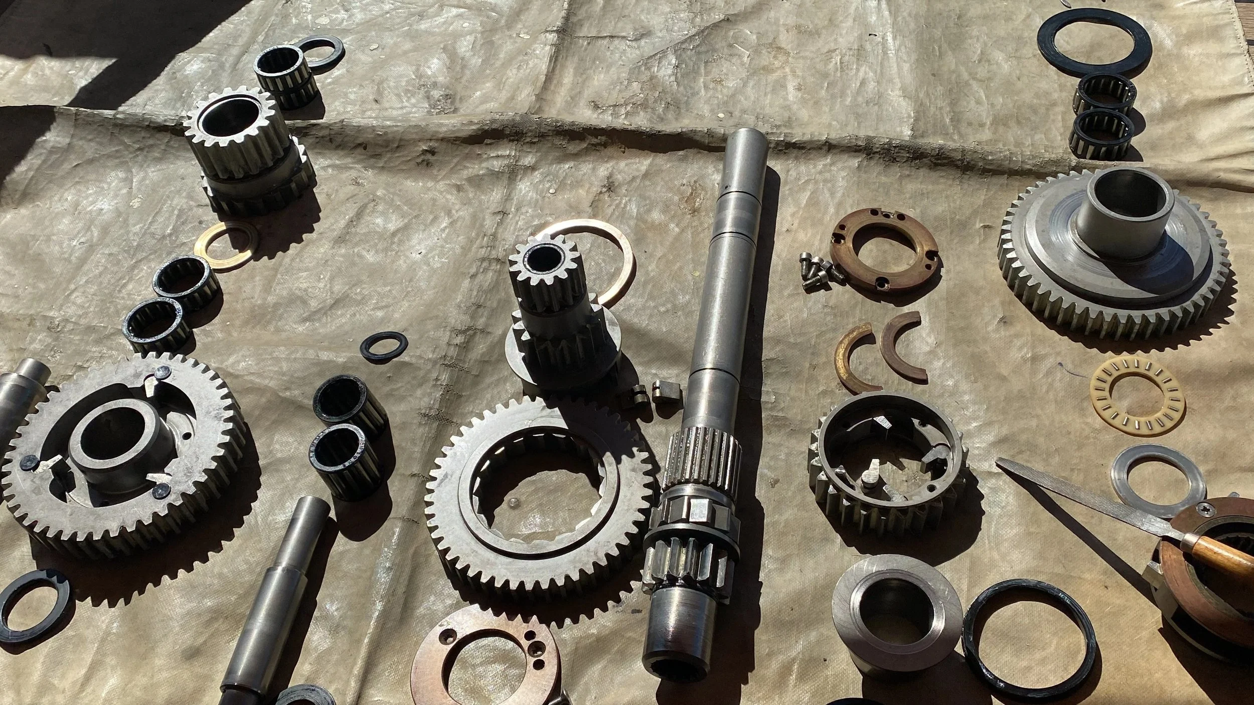 Various winch parts; metal gears, shafts, washers, and small mechanical parts laid out on a brown surface, with a pair of scissors nearby.