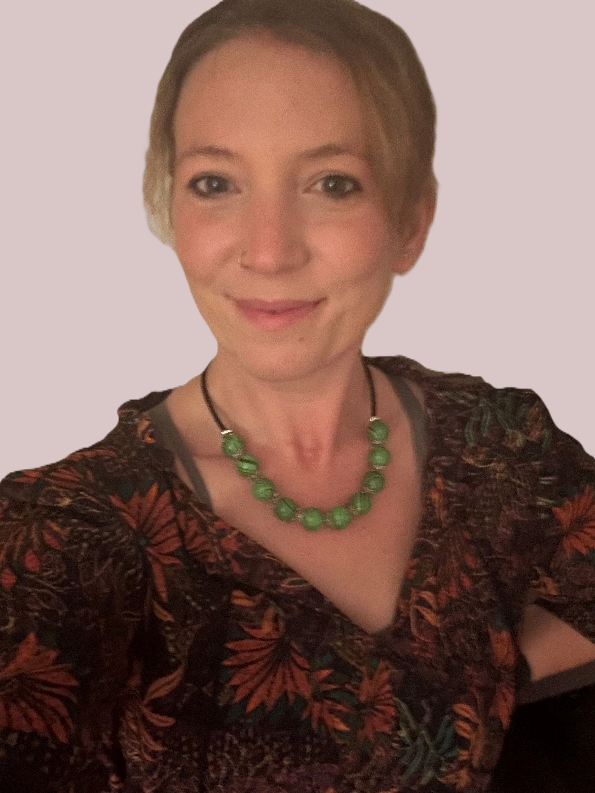 Headshot of Rhiannon Smith - a woman with short light brown hair, wearing a floral patterned top and a green beaded necklace, smiling at the camera.