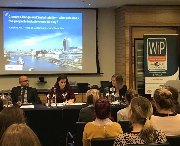 Panel discussion at a conference with a presentation slide titled 'Climate Change and Sustainability - what role does the property industry need to play?', featuring three speakers seated at a table, an audience listening, and a banner for the 'Natio