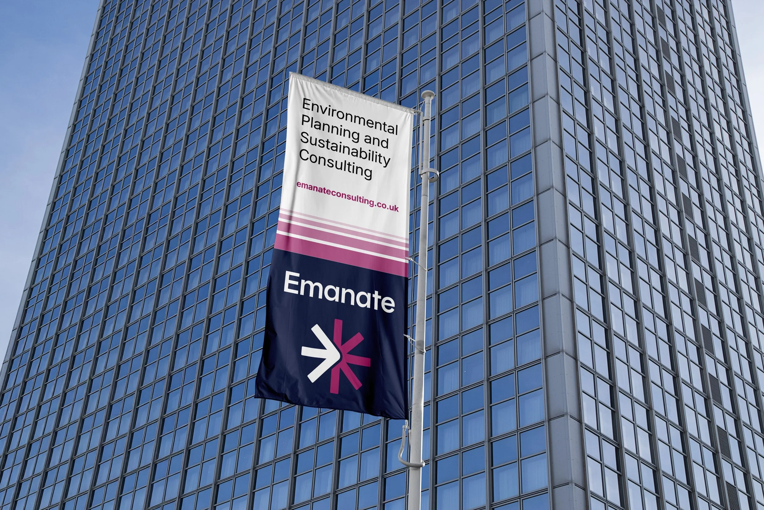 A banner for Emanate, an environmental planning and sustainability consulting company, hangs on a pole in front of a tall modern glass building.
