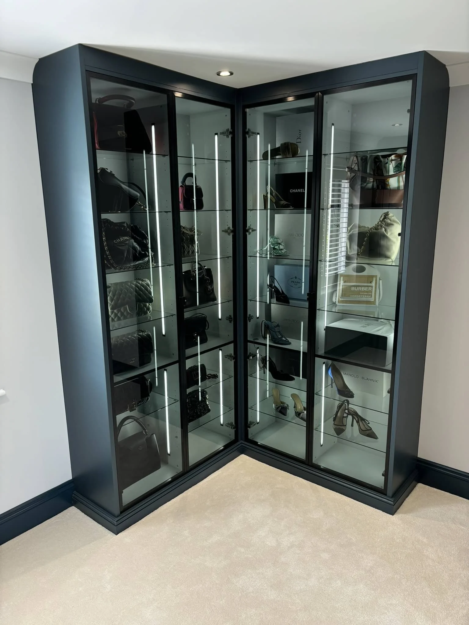 A corner display cabinet with glass doors and shelves, containing designer handbags, shoes, and accessories.