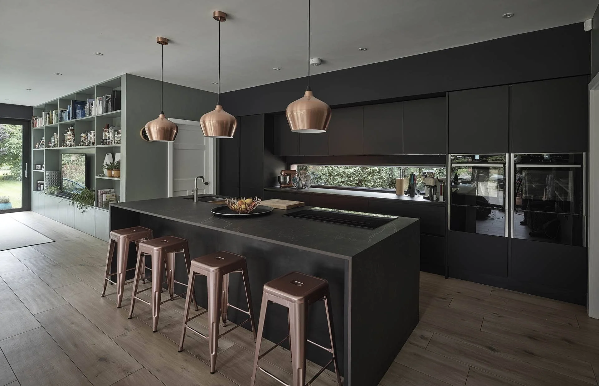 Modern kitchen with black cabinetry, a large island with bar stools, copper pendant lights, and built-in appliances.