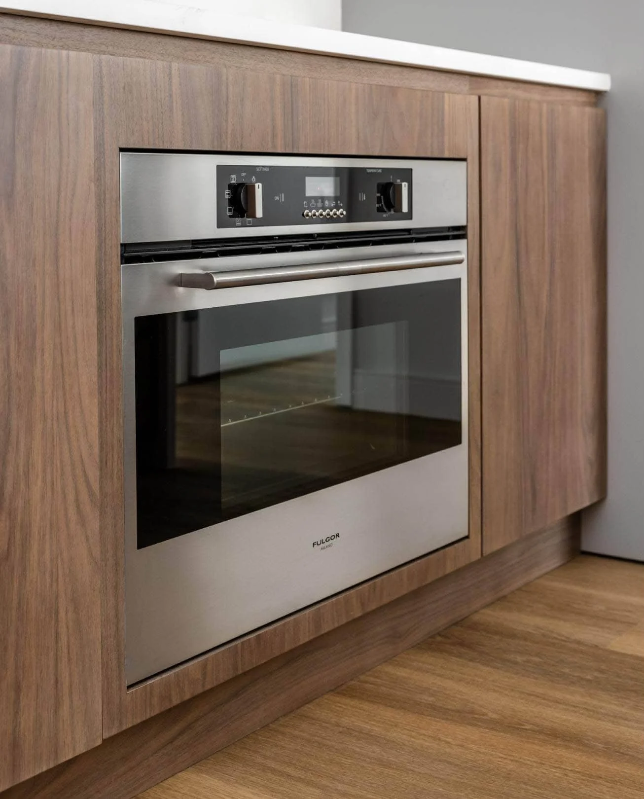 Stainless steel built-in oven with digital controls, installed in a wooden kitchen cabinet.