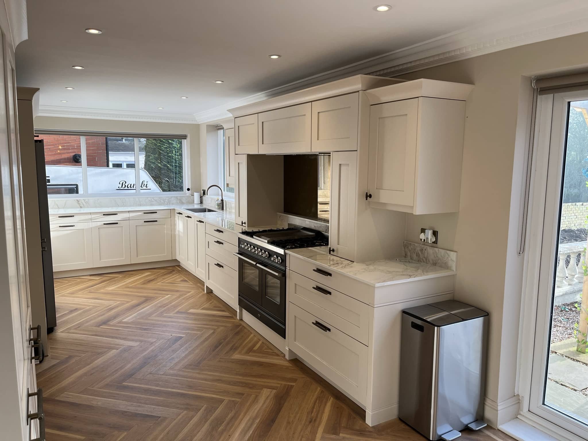 Modern kitchen with white cabinets, gray tiled backsplash, and a stovetop with two pots. Items on the countertop include jars, a white bowl, glassware, and containers.