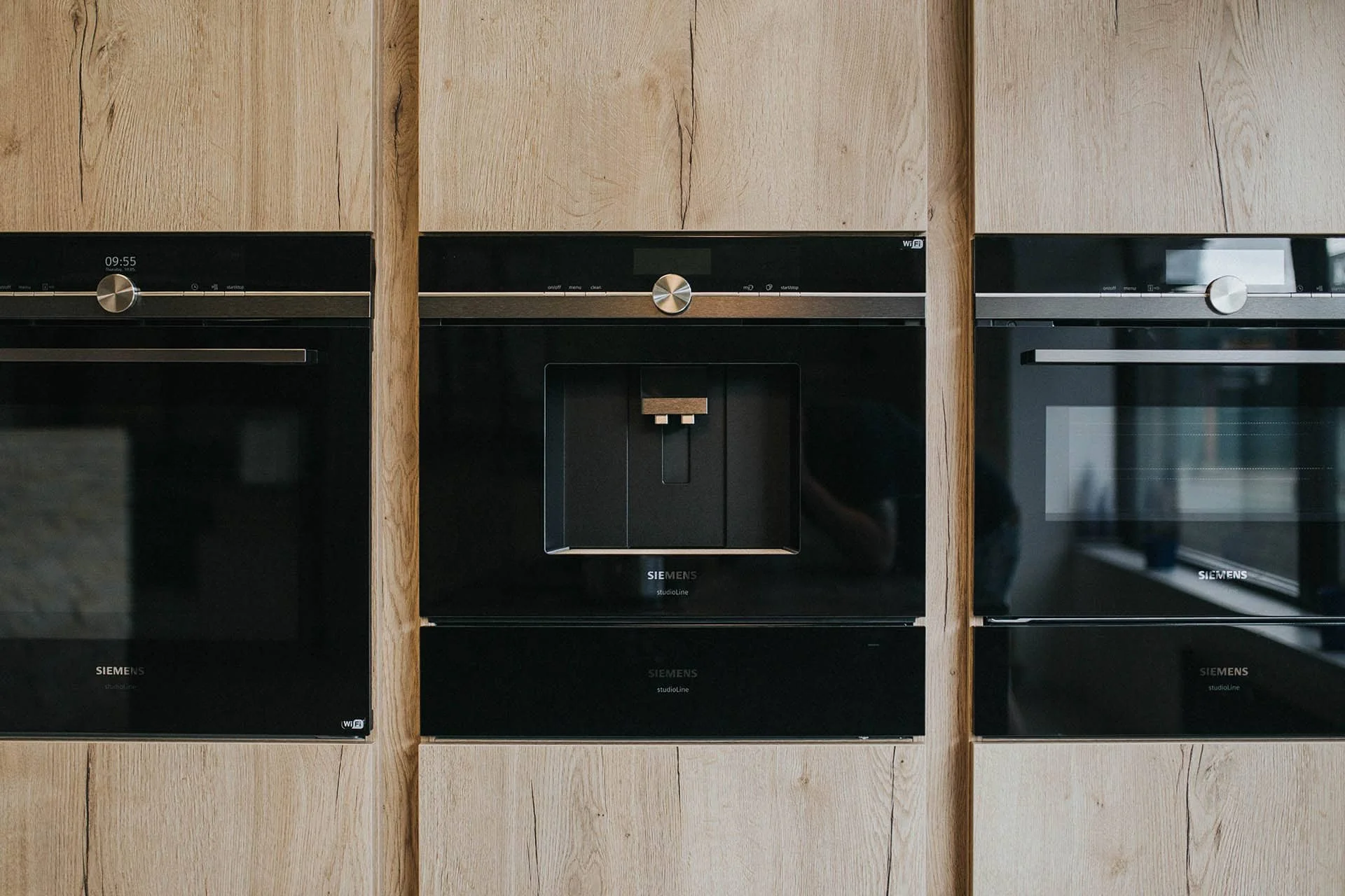 Three built-in black Siemens ovens installed in a wooden wall.