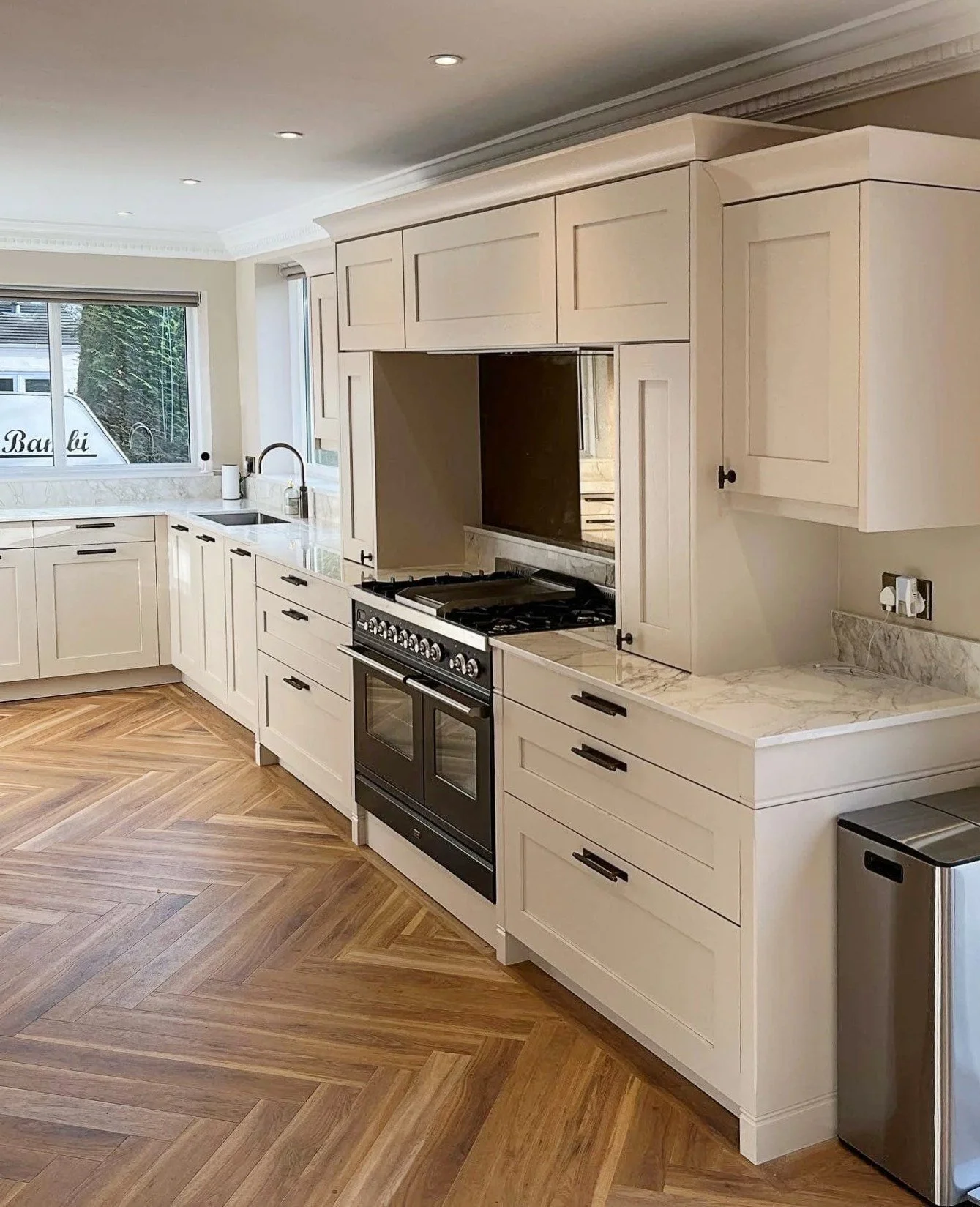 Modern kitchen with white cabinets, gray tiled backsplash, and a stovetop with two pots. Items on the countertop include jars, a white bowl, glassware, and containers.