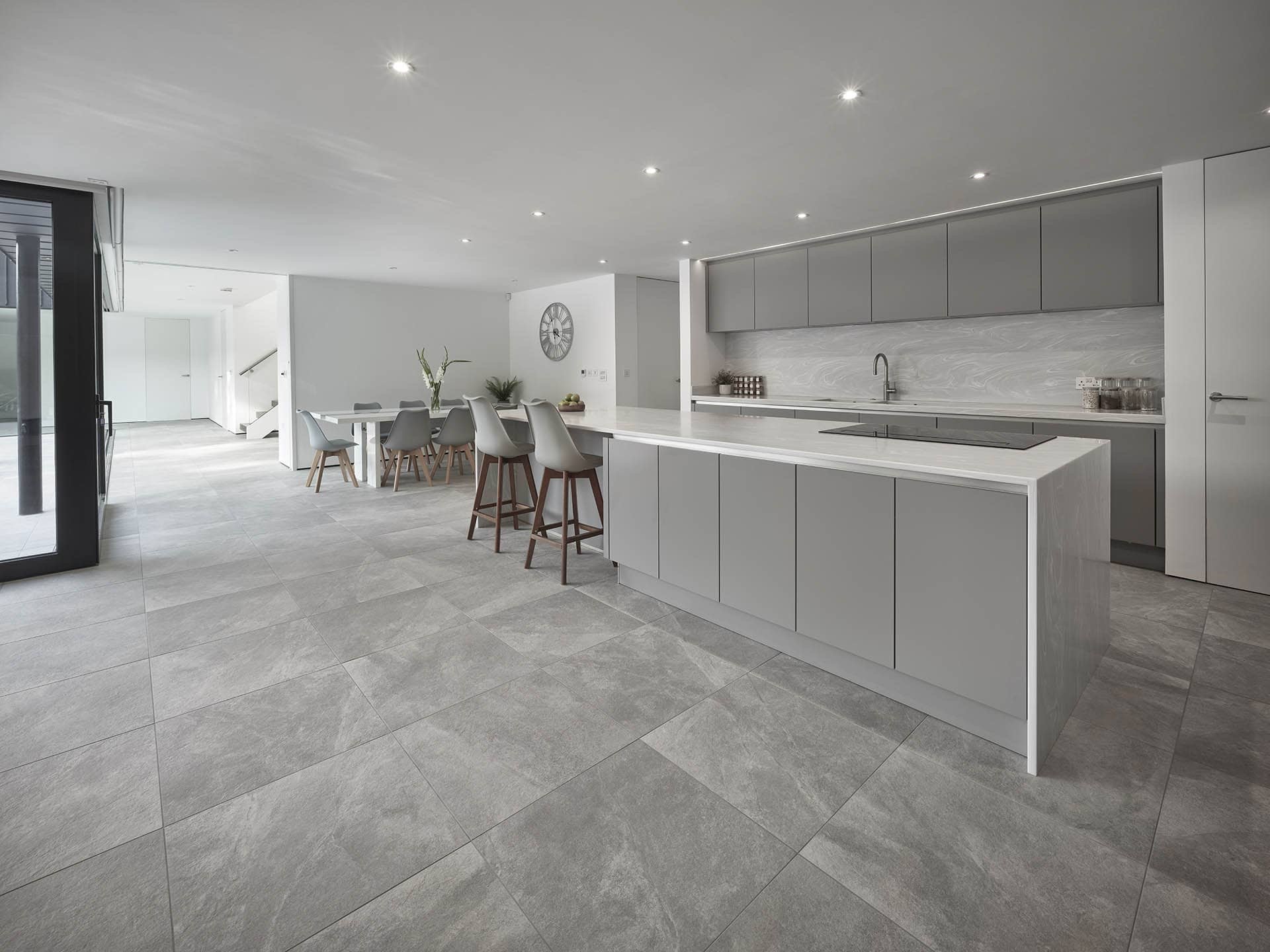 Modern kitchen and dining area with gray cabinets, a large island, and a dining table with eight chairs, lit by recessed ceiling lights.