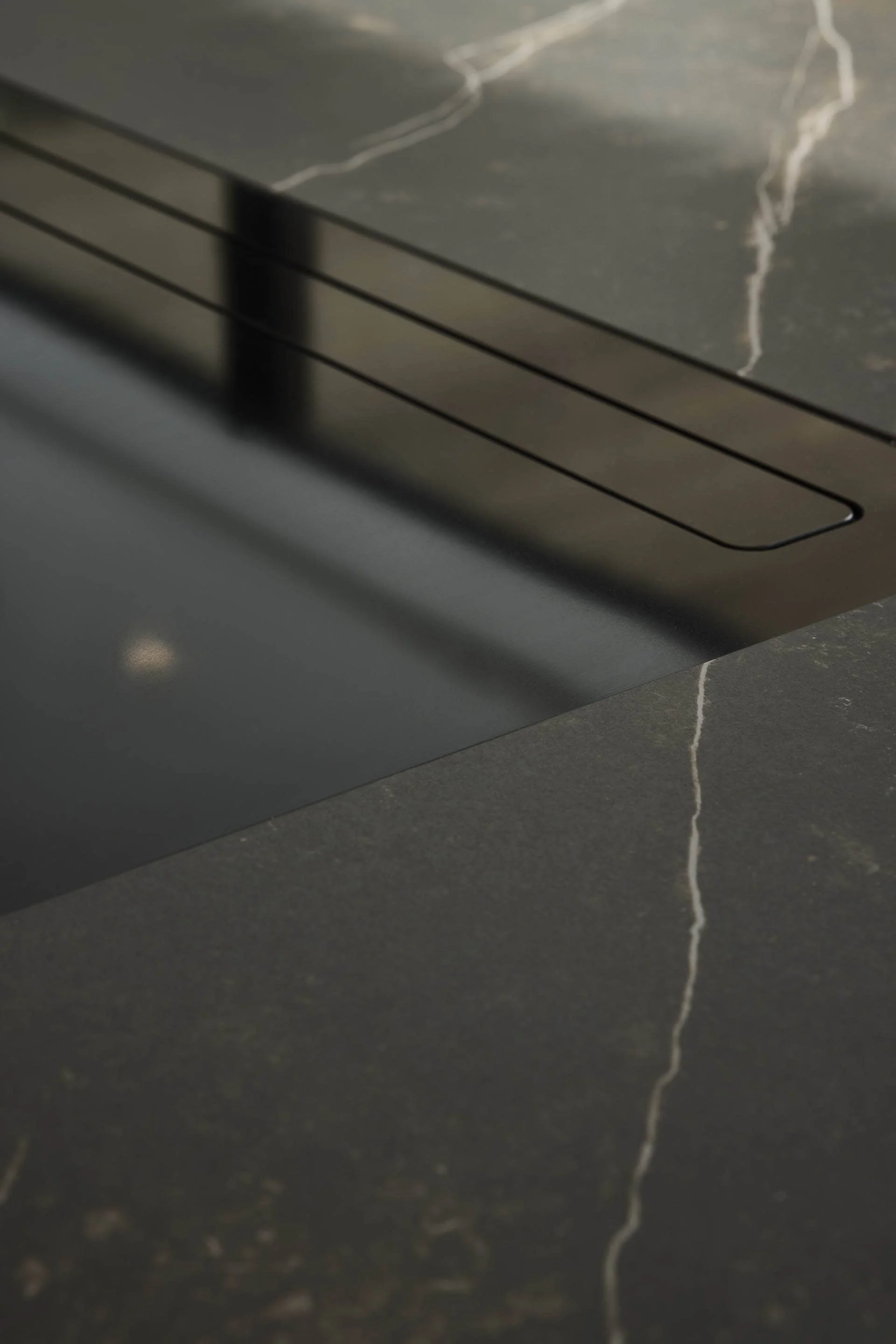Close-up of a black or dark gray marble countertop with white veining, and a section of a black appliance, possibly a stove or oven, with a vent or slot.