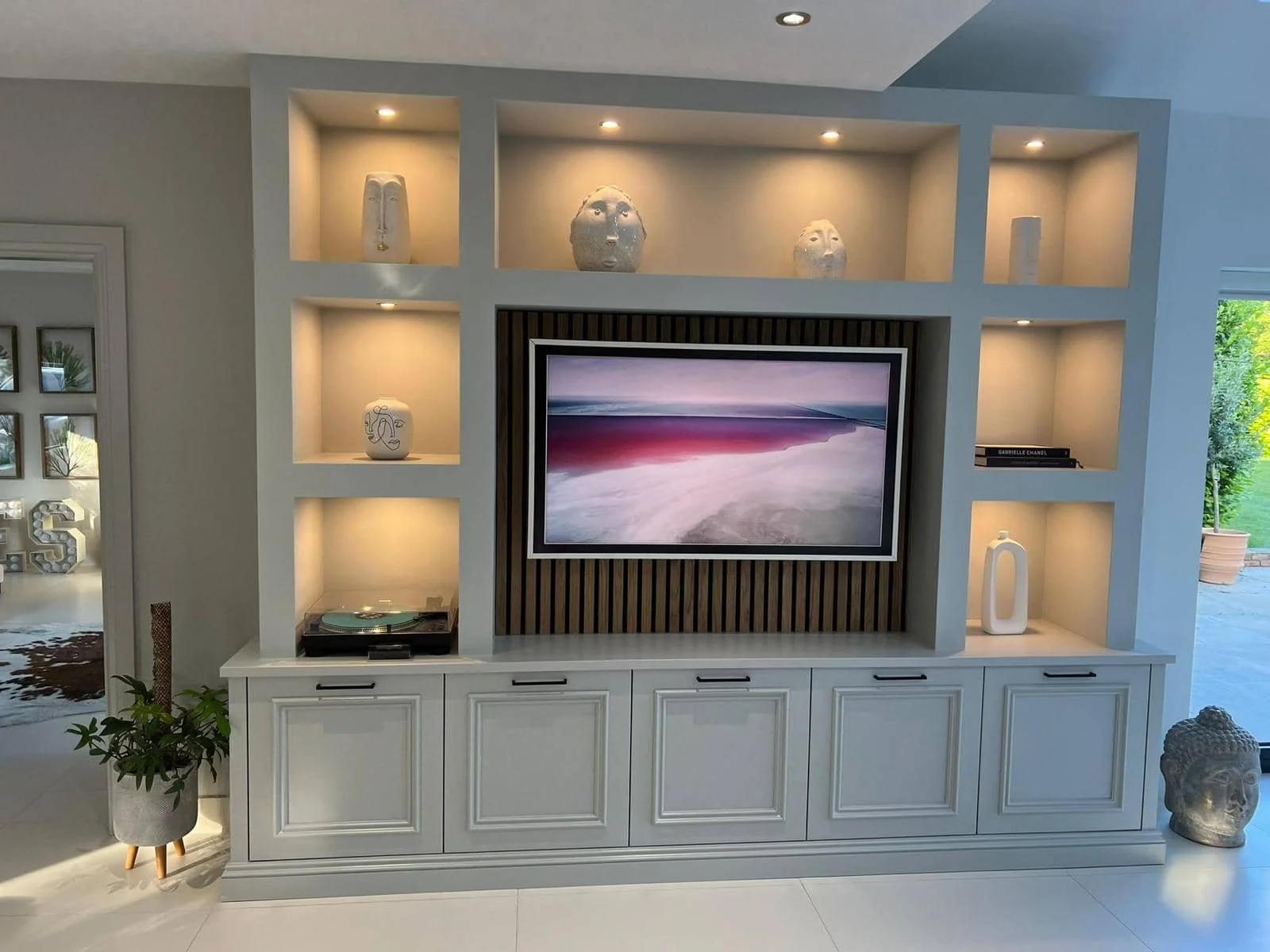 Living room entertainment center with decorative vases, books, a potted plant, and a Buddha head sculpture.