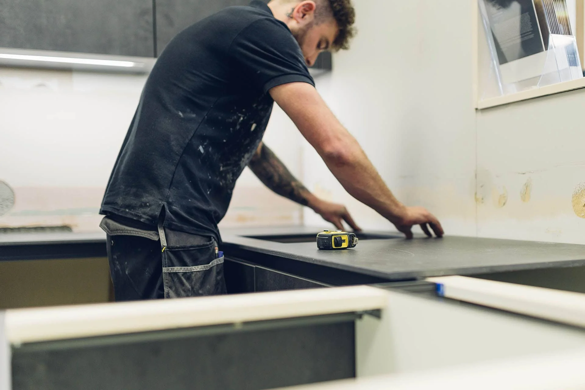 A man working on a kitchen renovation, measuring and preparing a black countertop, with a tape measure placed on it.