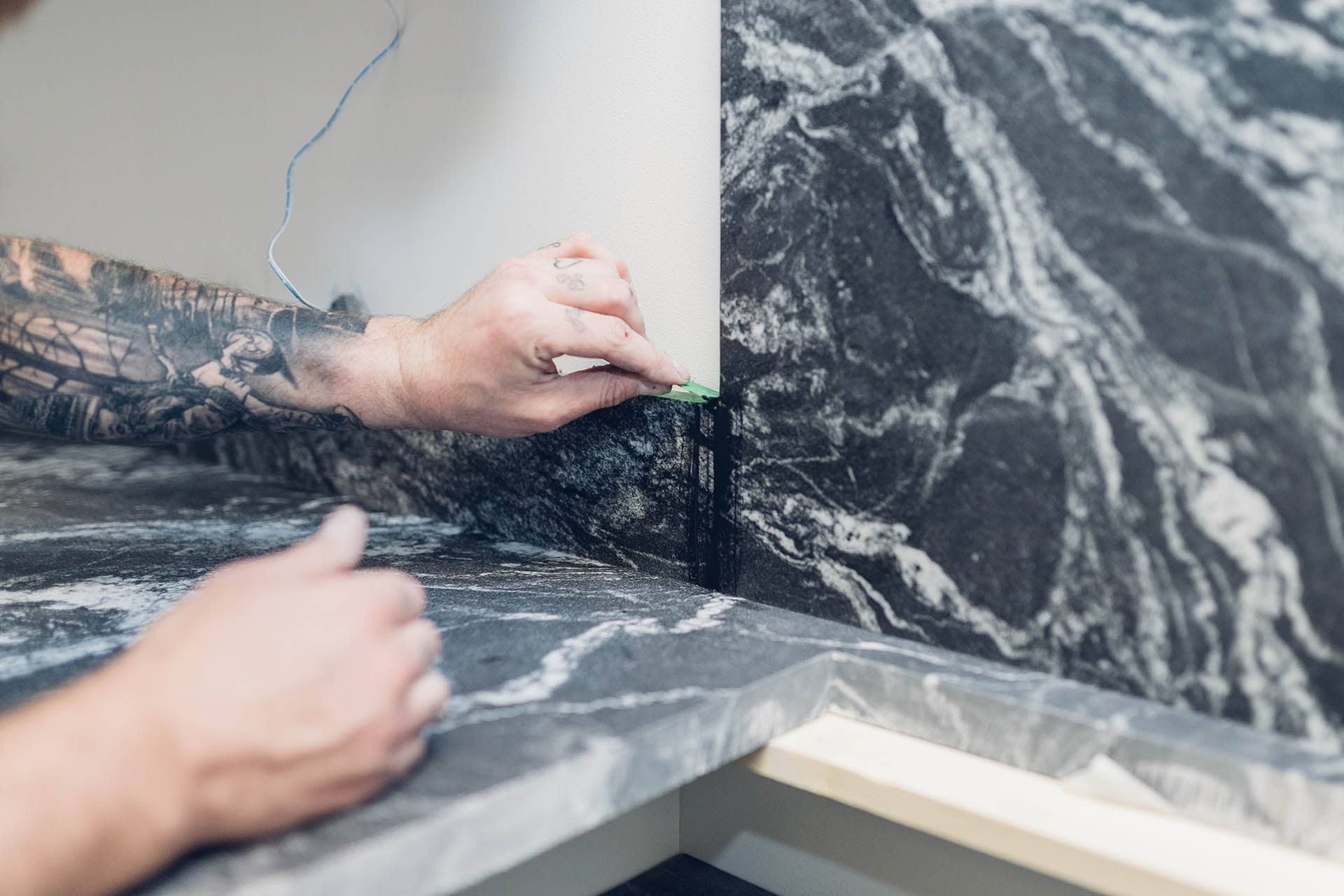 Person installing black marble tiles with white veins on a wall, using a notched trowel