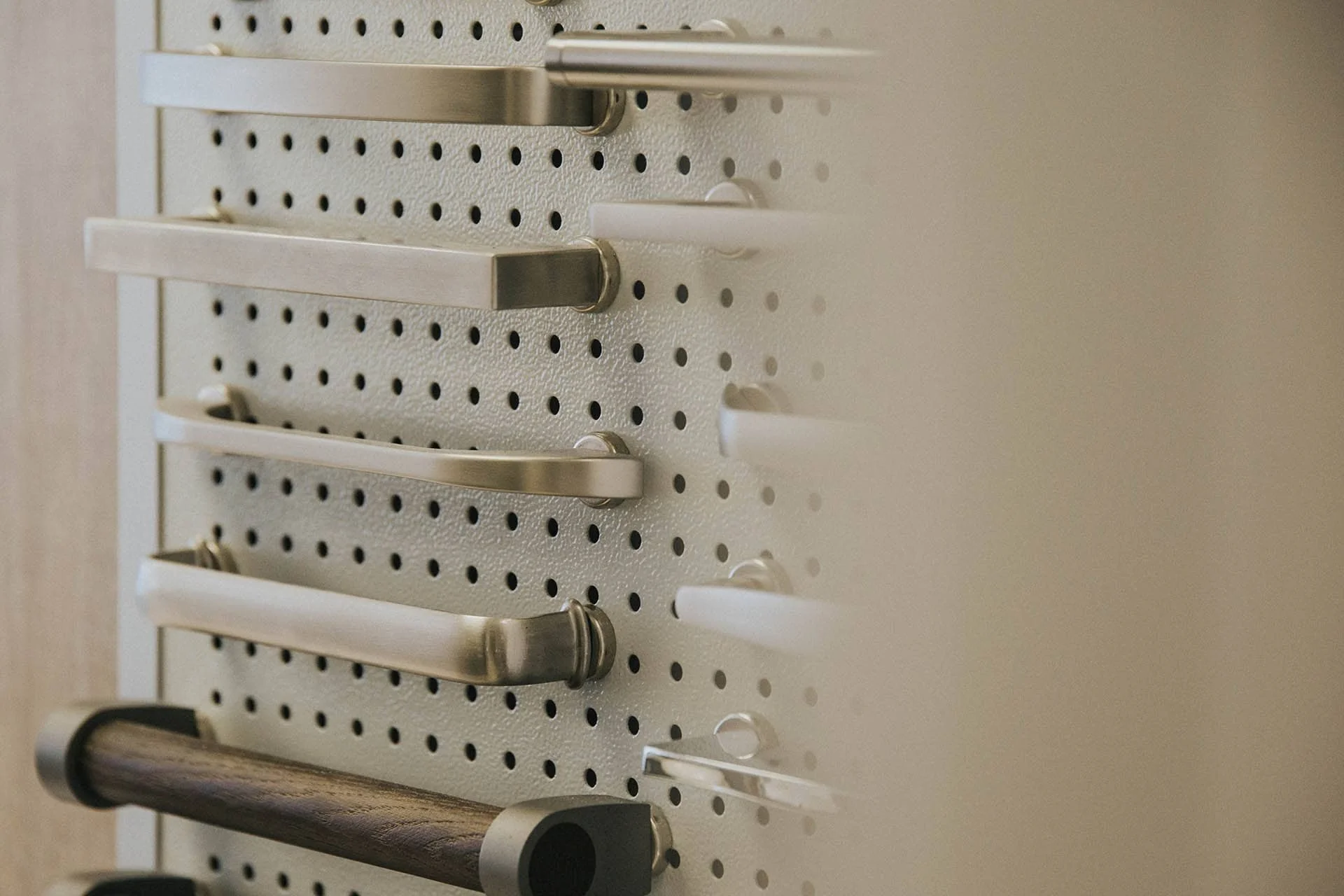 Various grab bars and handles mounted on a perforated white wall panel. Kitchen showroom handle display.