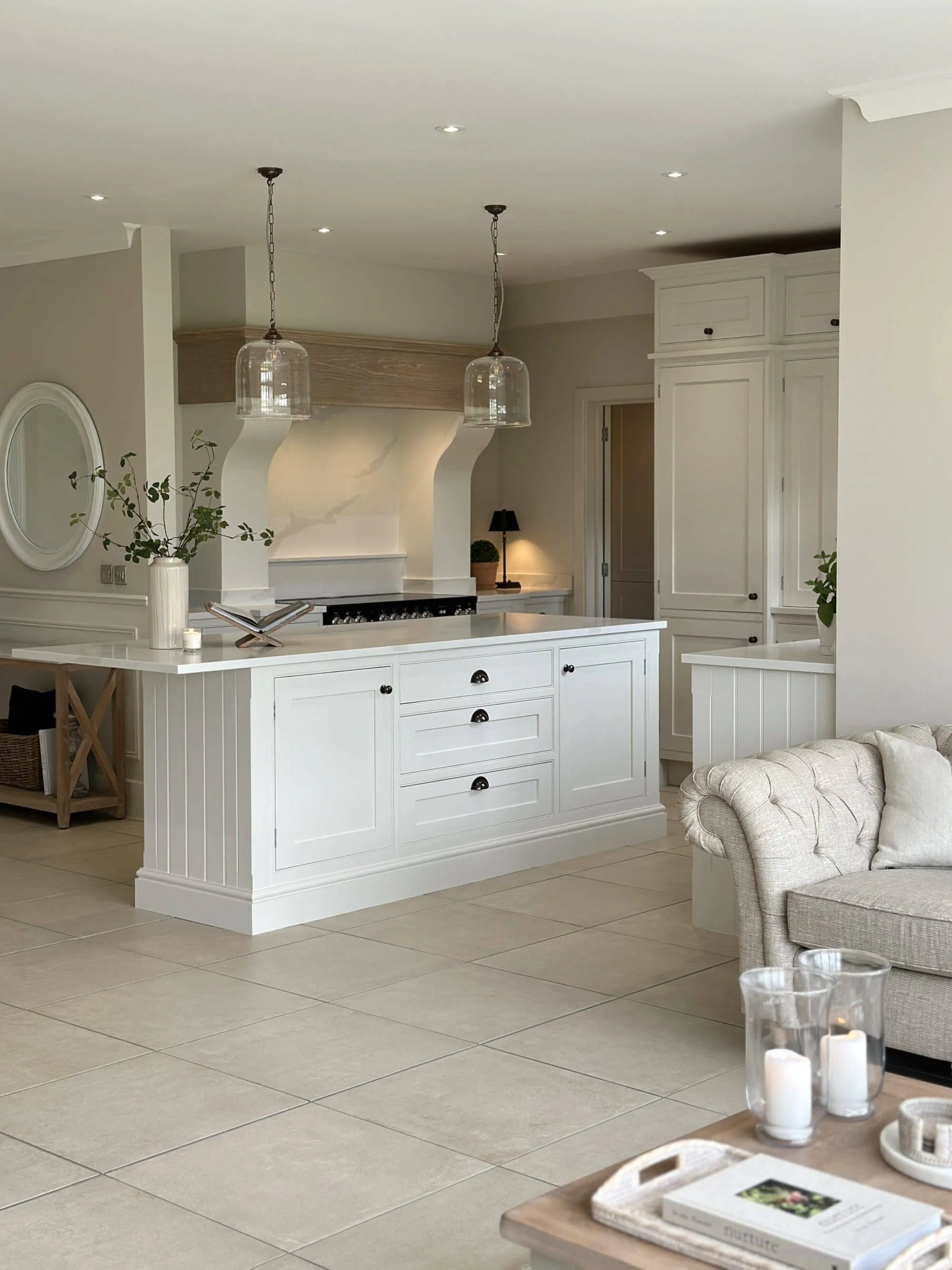 Modern kitchen with white cabinets, a central island, beige tiled floors, and glass pendant lights hanging from the ceiling.