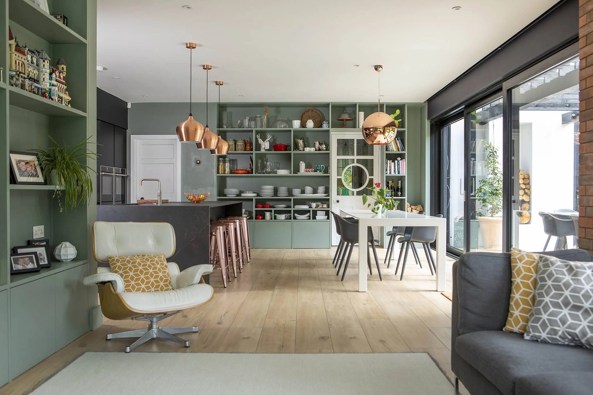 Open-concept kitchen and living room with green cabinetry, a white dining table, gray chairs, black sliding doors, and modern decor.