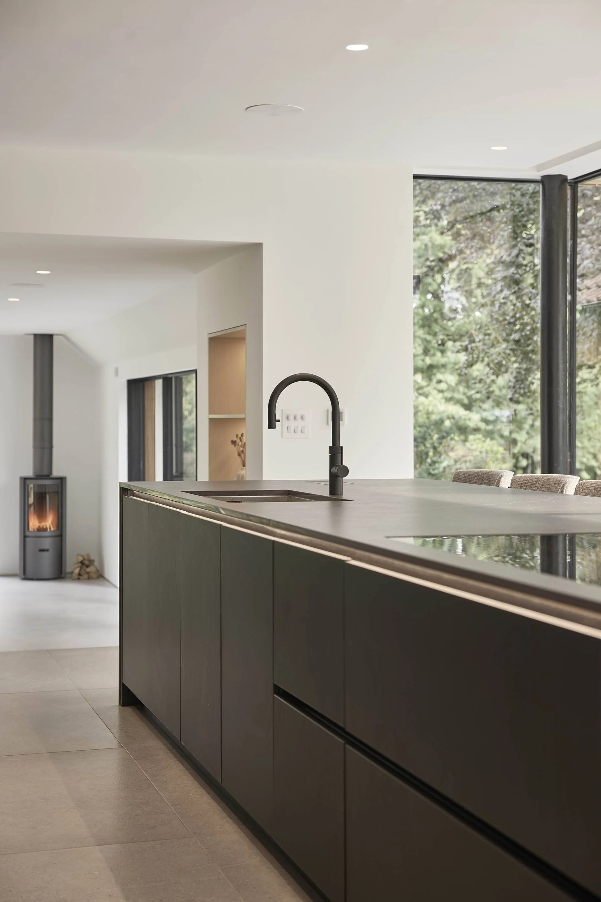 Modern kitchen island with black cabinetry, a black faucet, and a built-in sink, adjacent to large windows overlooking greenery.