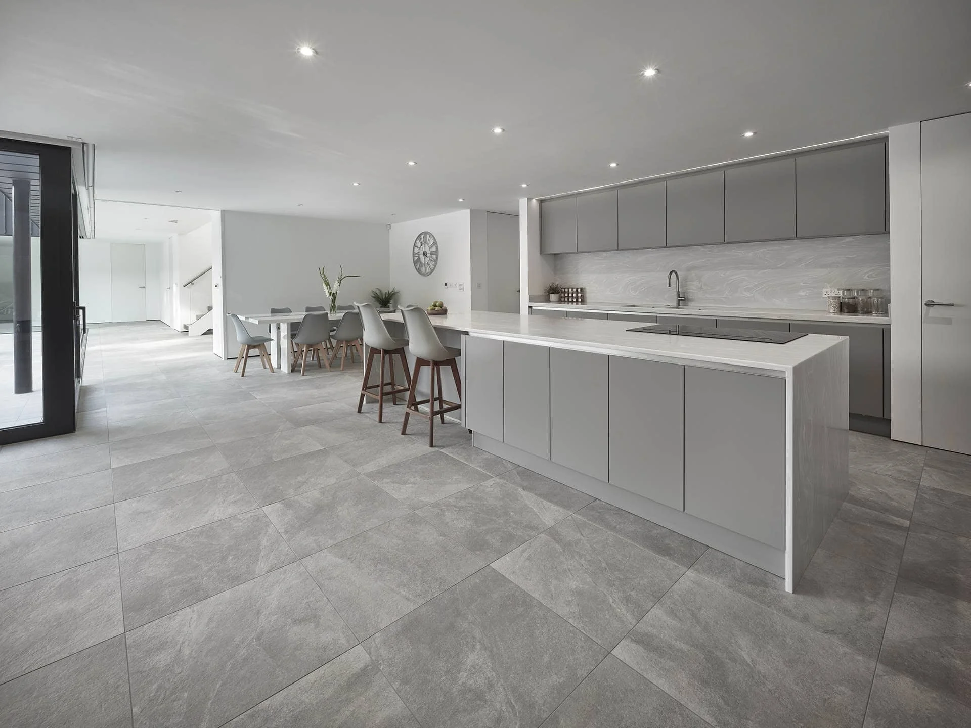 Modern, minimalist open-plan kitchen with gray cabinets, white countertops, a large island with seating, and a dining area with gray chairs and a round table.