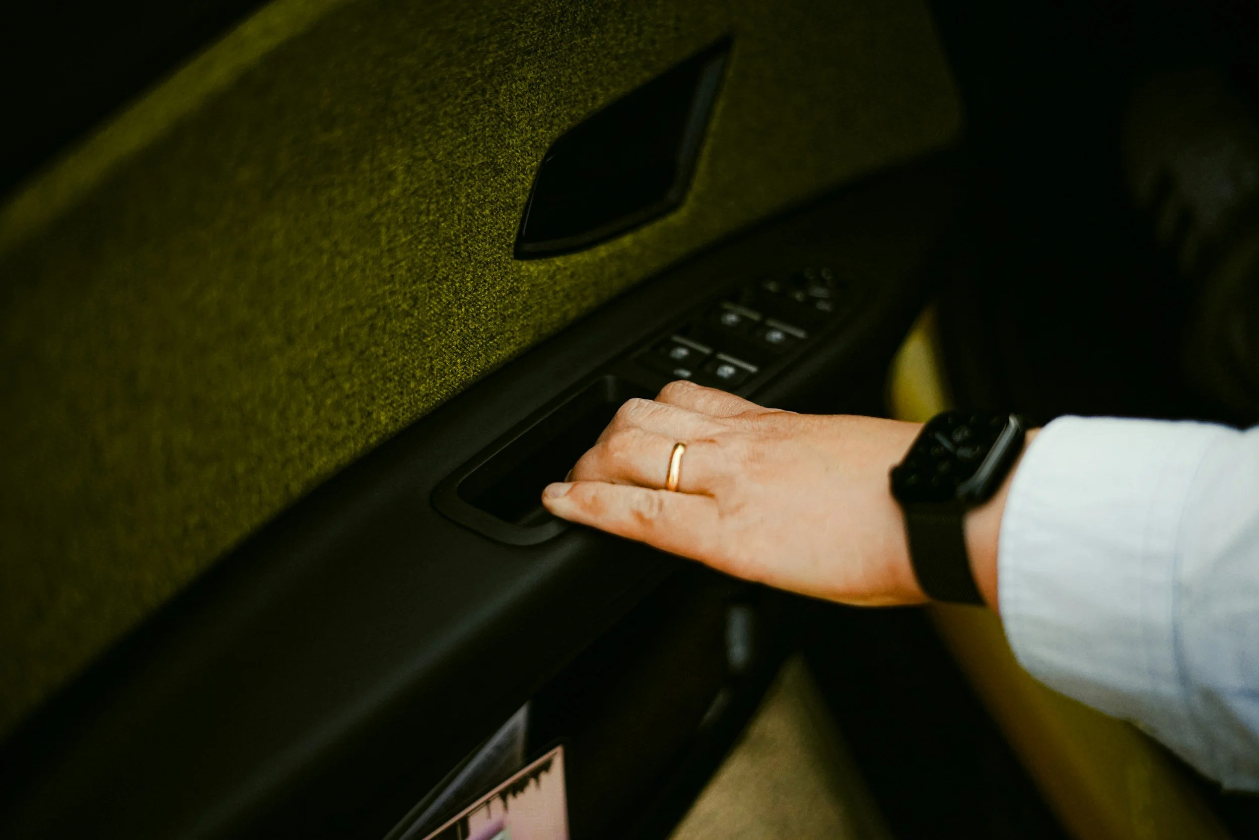 Person with a watch and wedding ring adjusting window controls in a car.