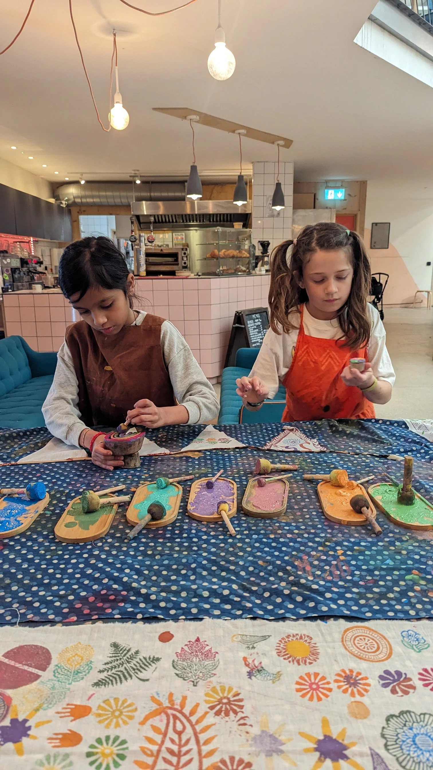 Two young girls engaged in the process of painting and creating block print clothing,. learning how to make indian inspired patterns in studio om workshop.