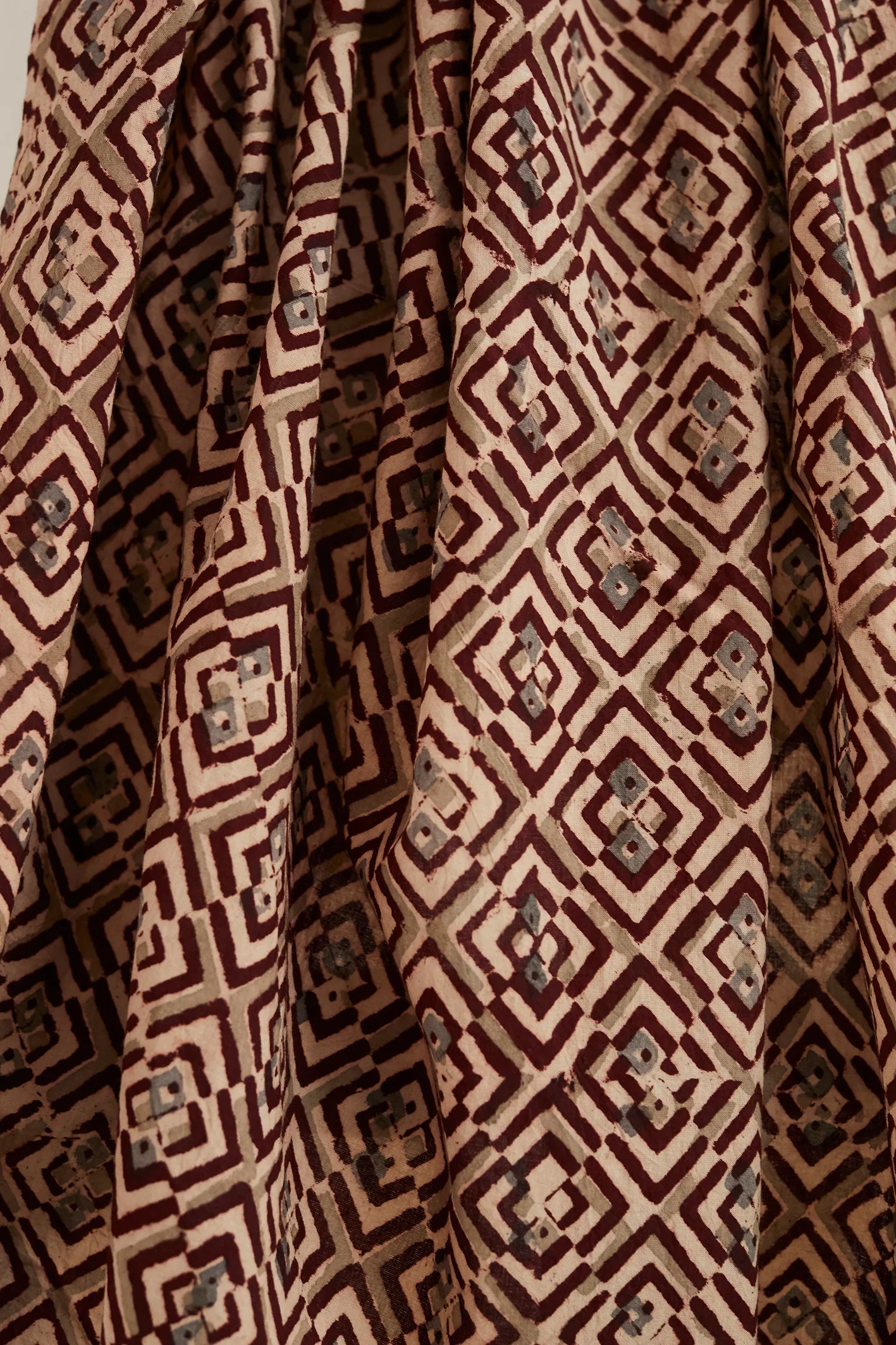 Close-up view of fabric with a geometric pattern of diamond shapes in beige, dark red, and small gray accents.