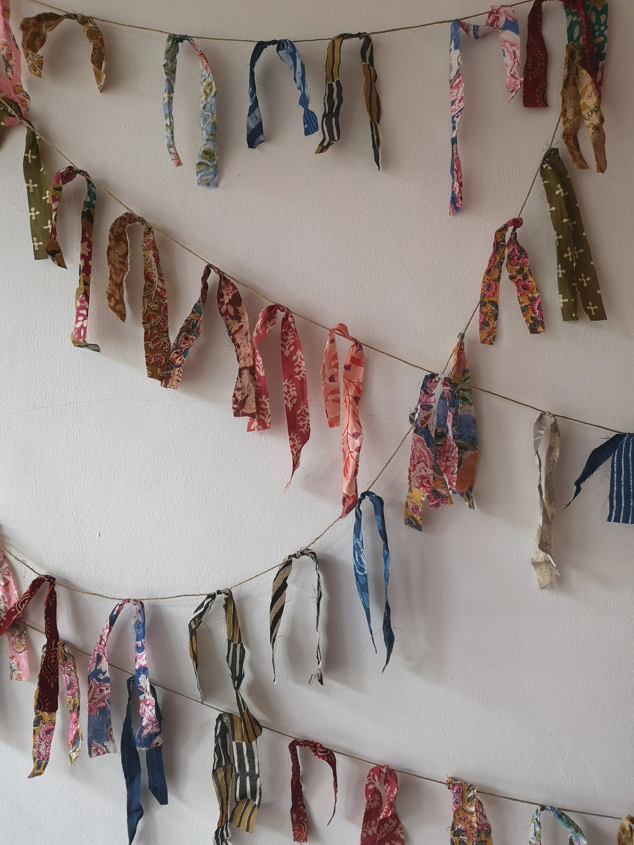 Multicolored fabric ribbons tied to string, hanging on a white wall.