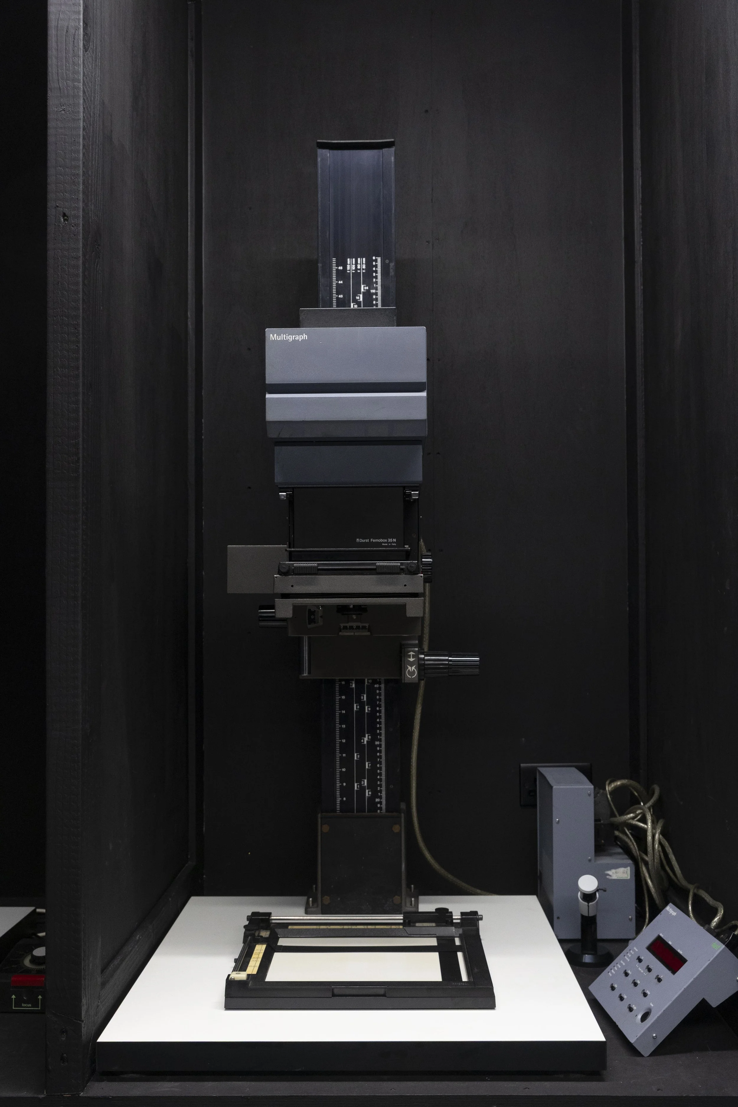 Photograph of a primary calibration system for a multigraph, including a black metal frame, a white table, a calibration chart, and electronic control devices, all set up in a black enclosure.