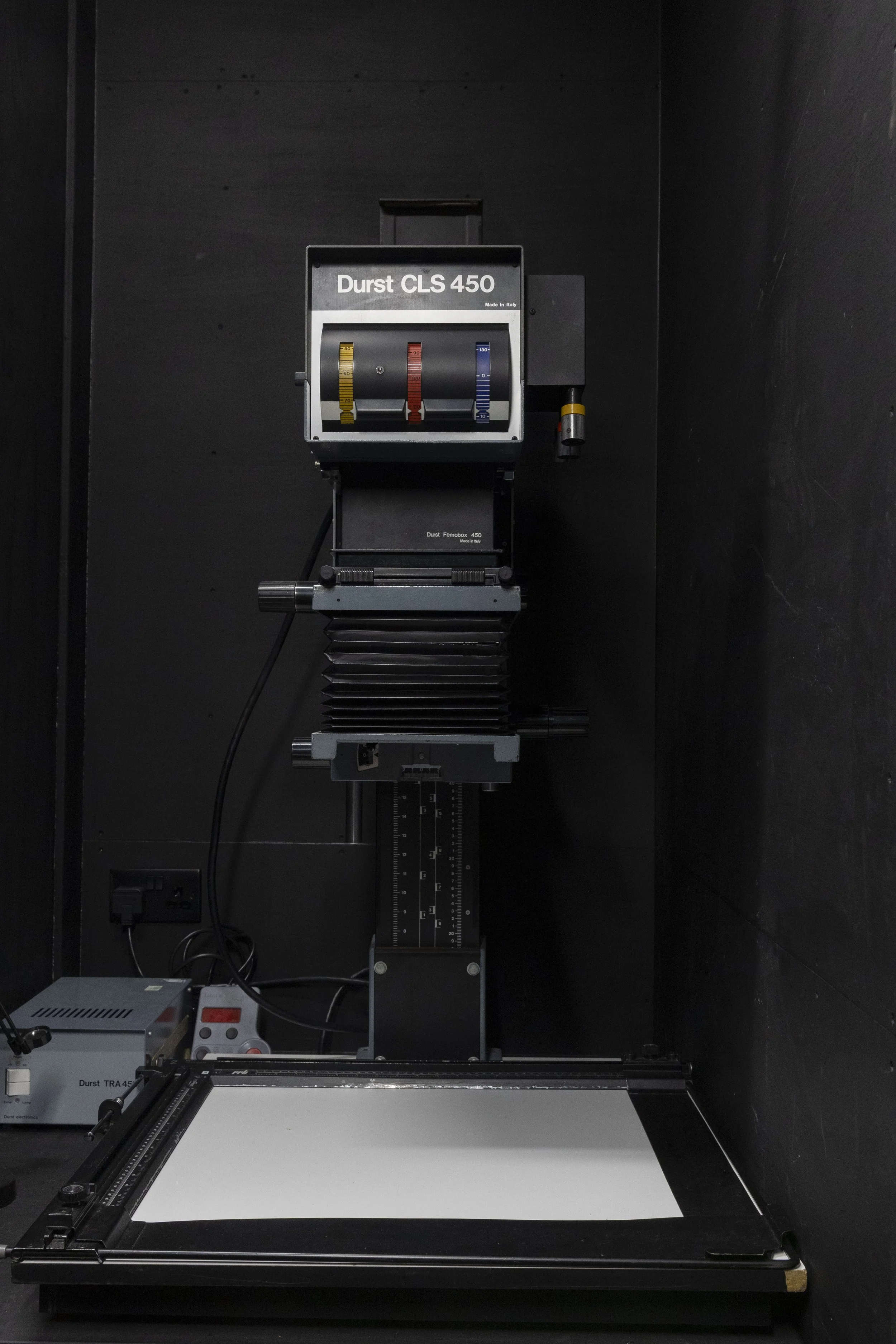 Laboratory testing machine with a white testing surface, mechanical components, and digital controls in a dark room.