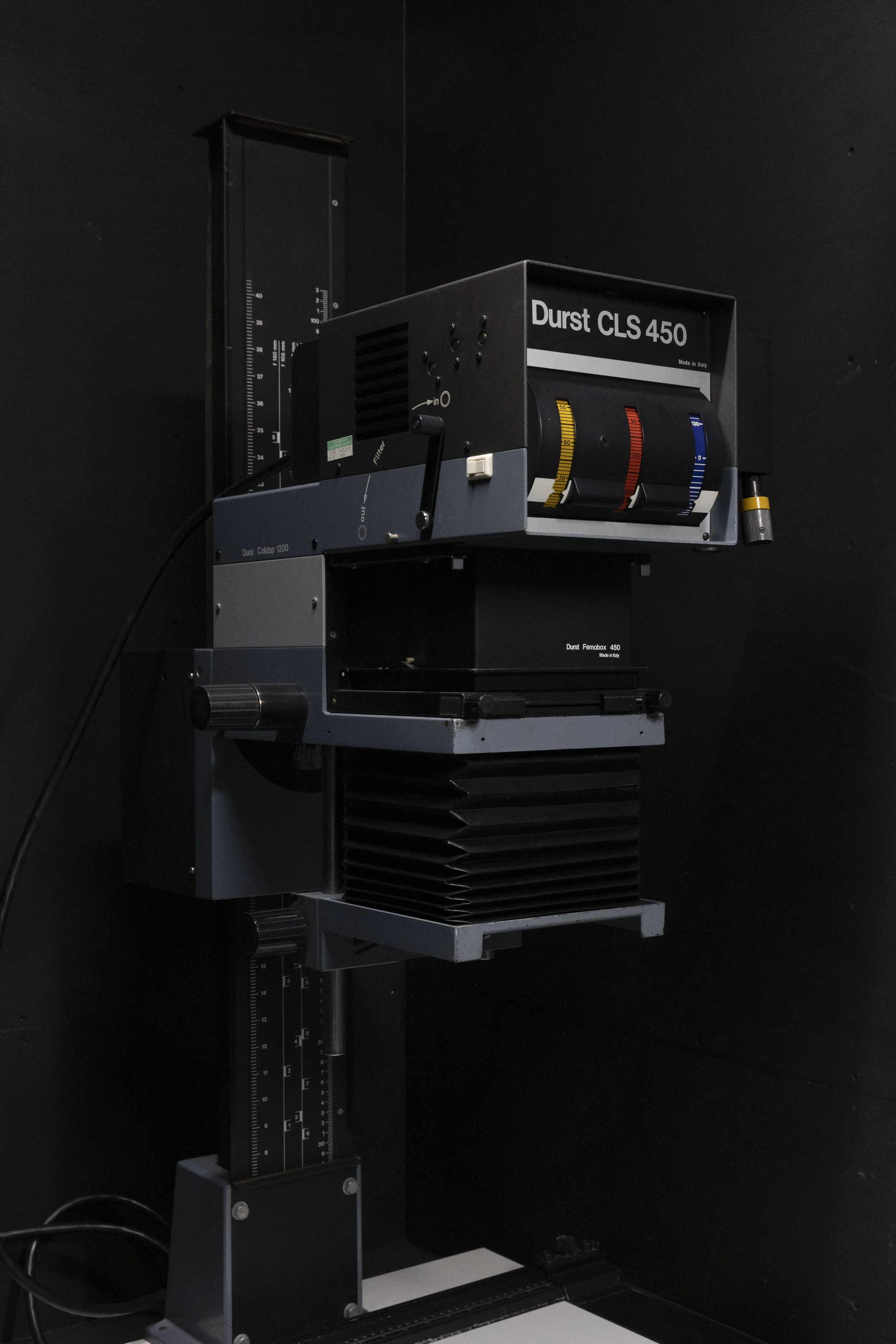 A scientific or laboratory device labeled Durst CLS 450, used for precise measurement or testing, mounted on a stand with a vertical measurement scale in the background.