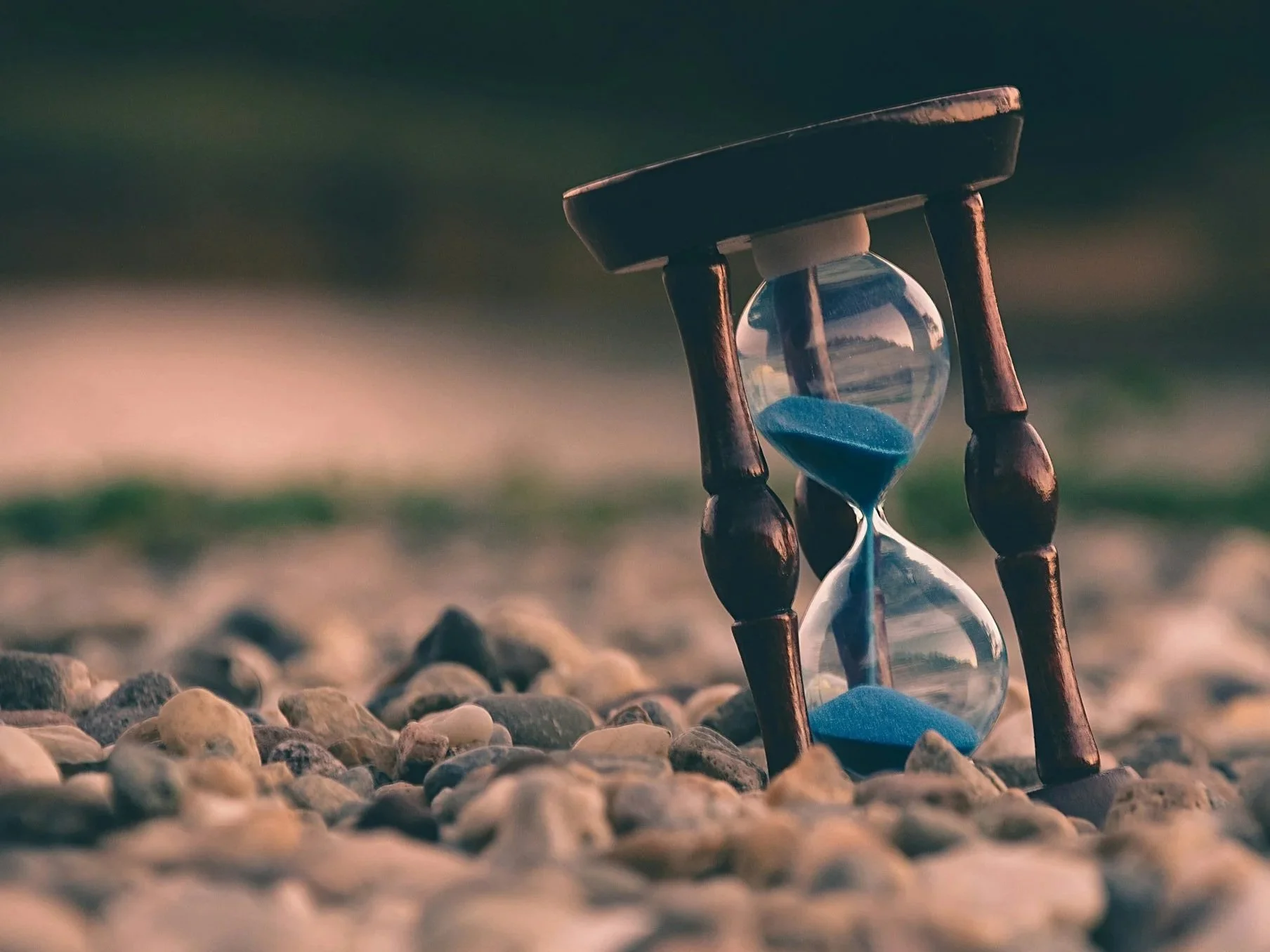 Un reloj de arena con arena azul, colocado sobre piedras.