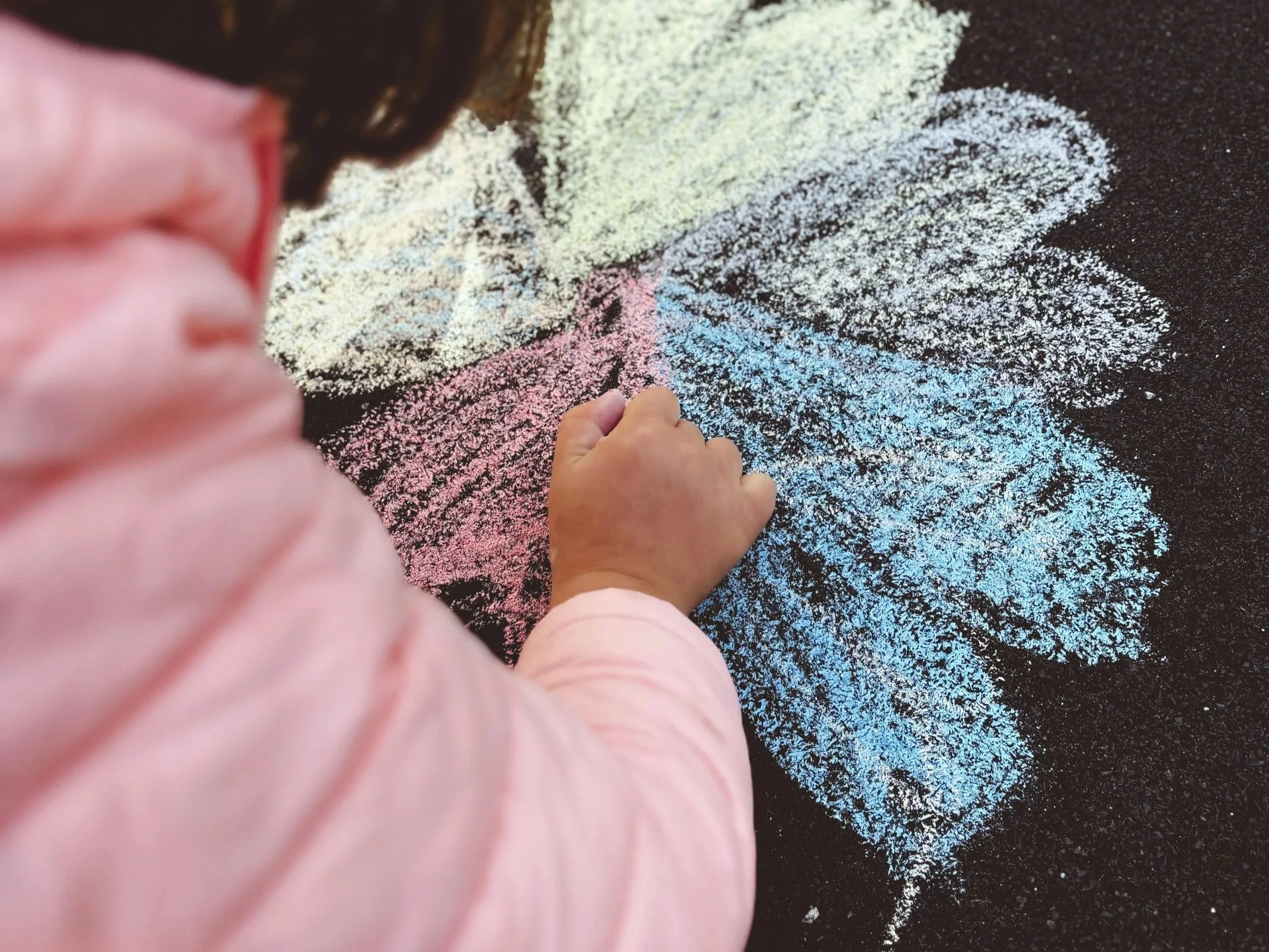 Niña dibujando con tizas de colores en una pizarra negra