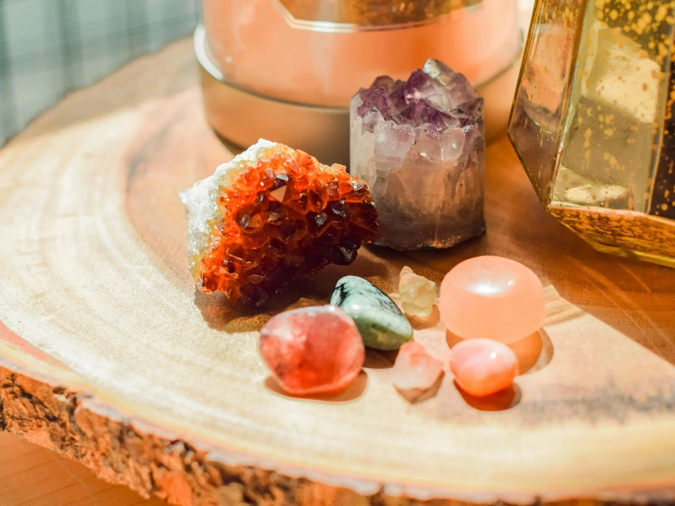 Variedad de cristales y piedras preciosas sobre una sección de tronco de árbol, con un fondo neutro y objetos decorativos en el entorno.