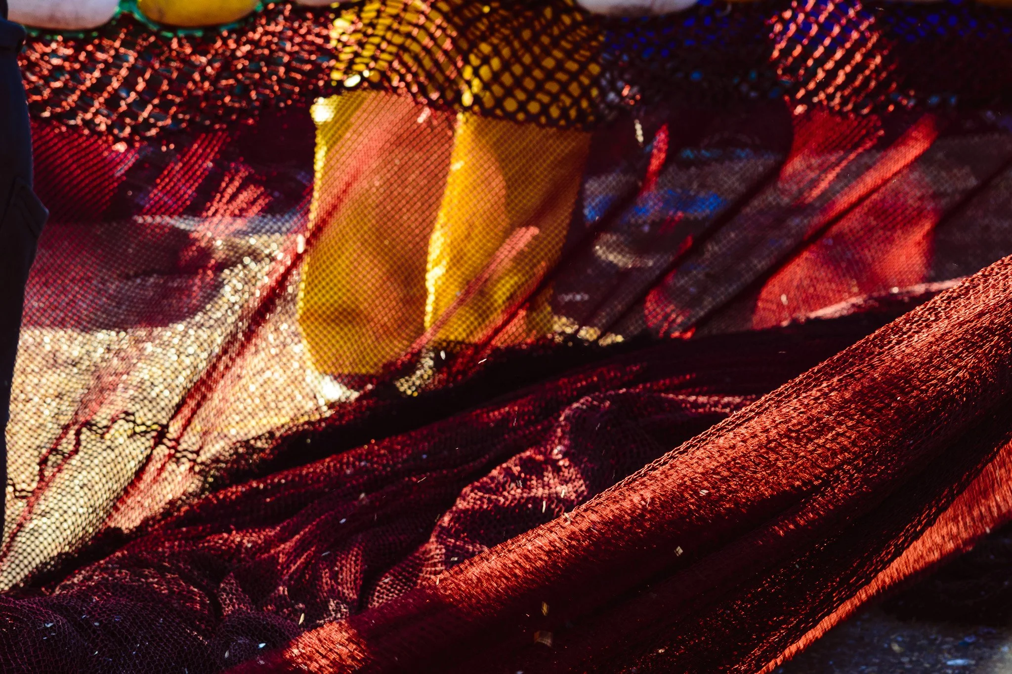 Close-up of shimmering red, yellow, and black fabric with intricate textures and patterns, illuminated to highlight its glossy and layered surface.