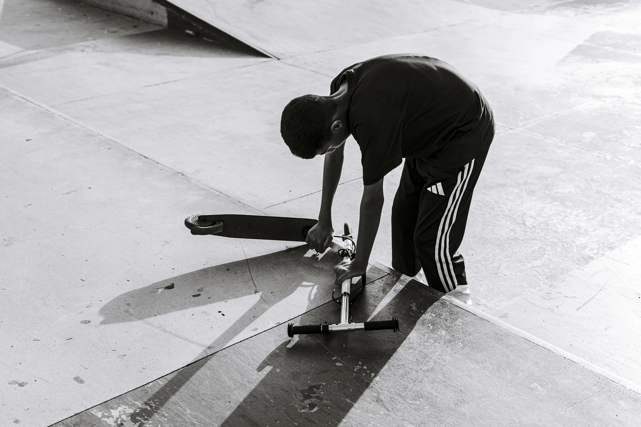 Person repairing a scooter at a concrete skate park