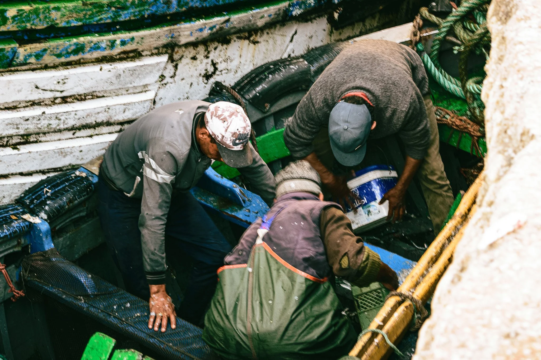 Four people working inside a large, metal boat with various ropes and equipment.