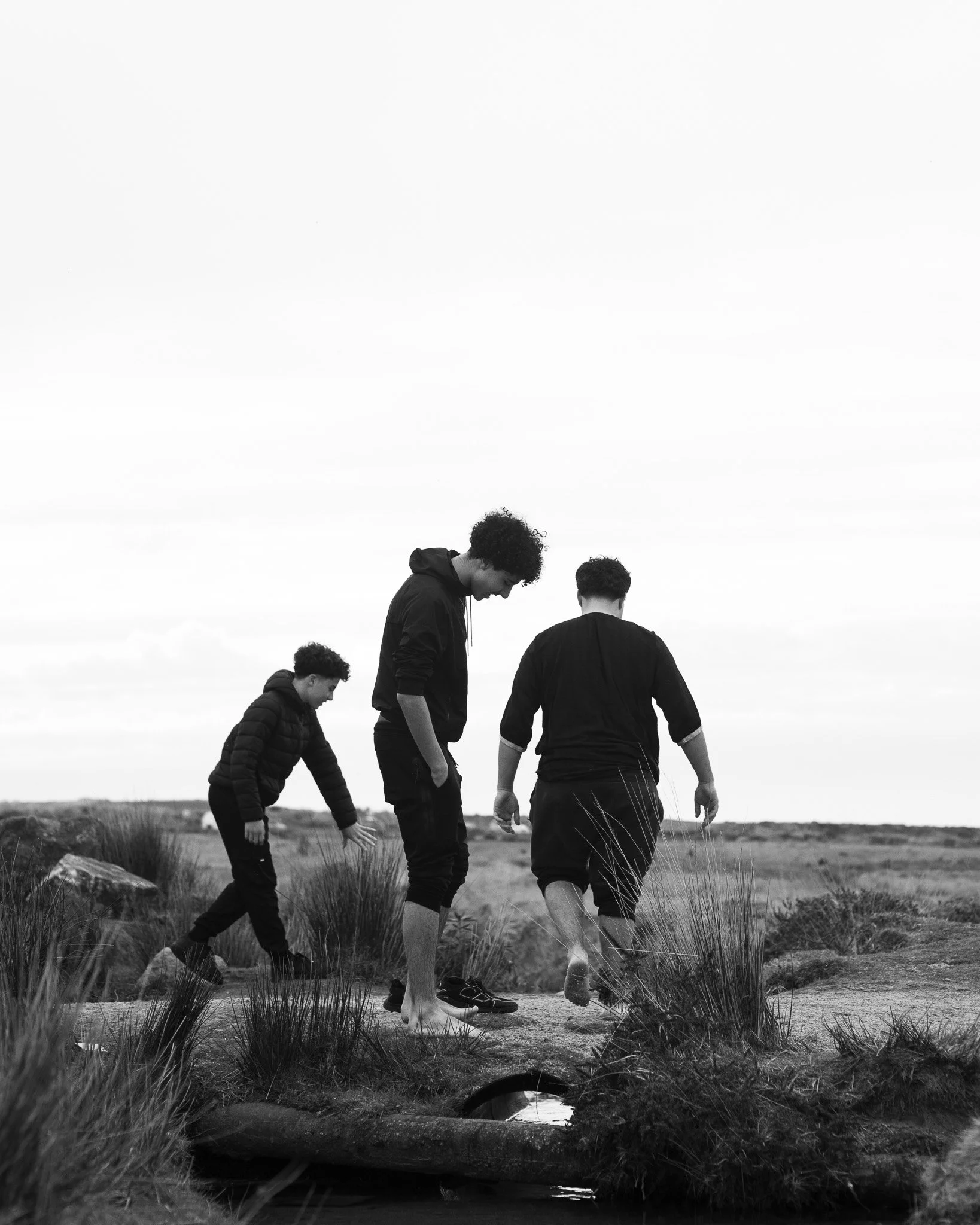 Four people walking on a sandy trail through grass and dunes, with cloudy sky above; black and white photo.