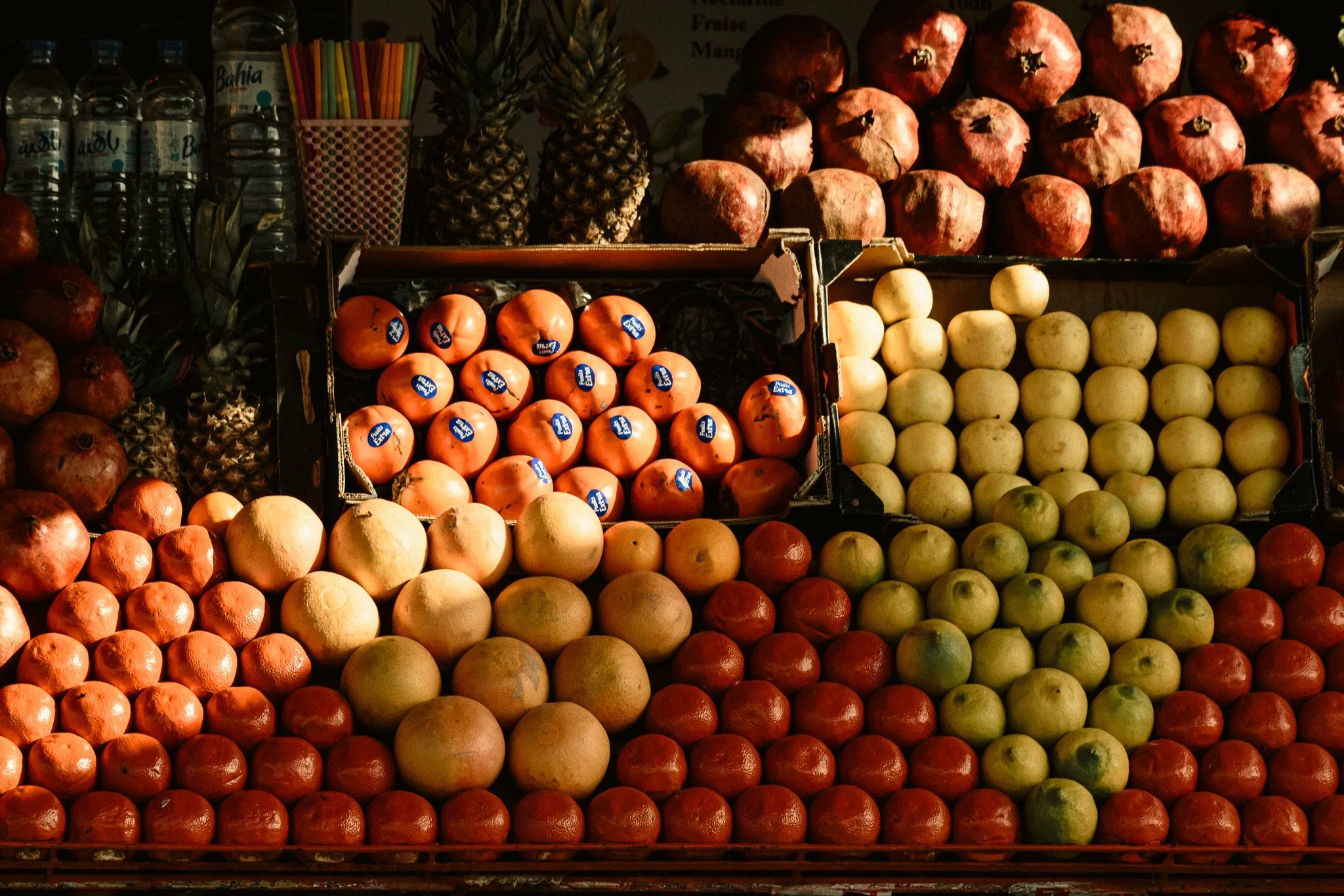 Display of various fruits including pineapples, pomegranates, oranges, and apples on a market stall.
